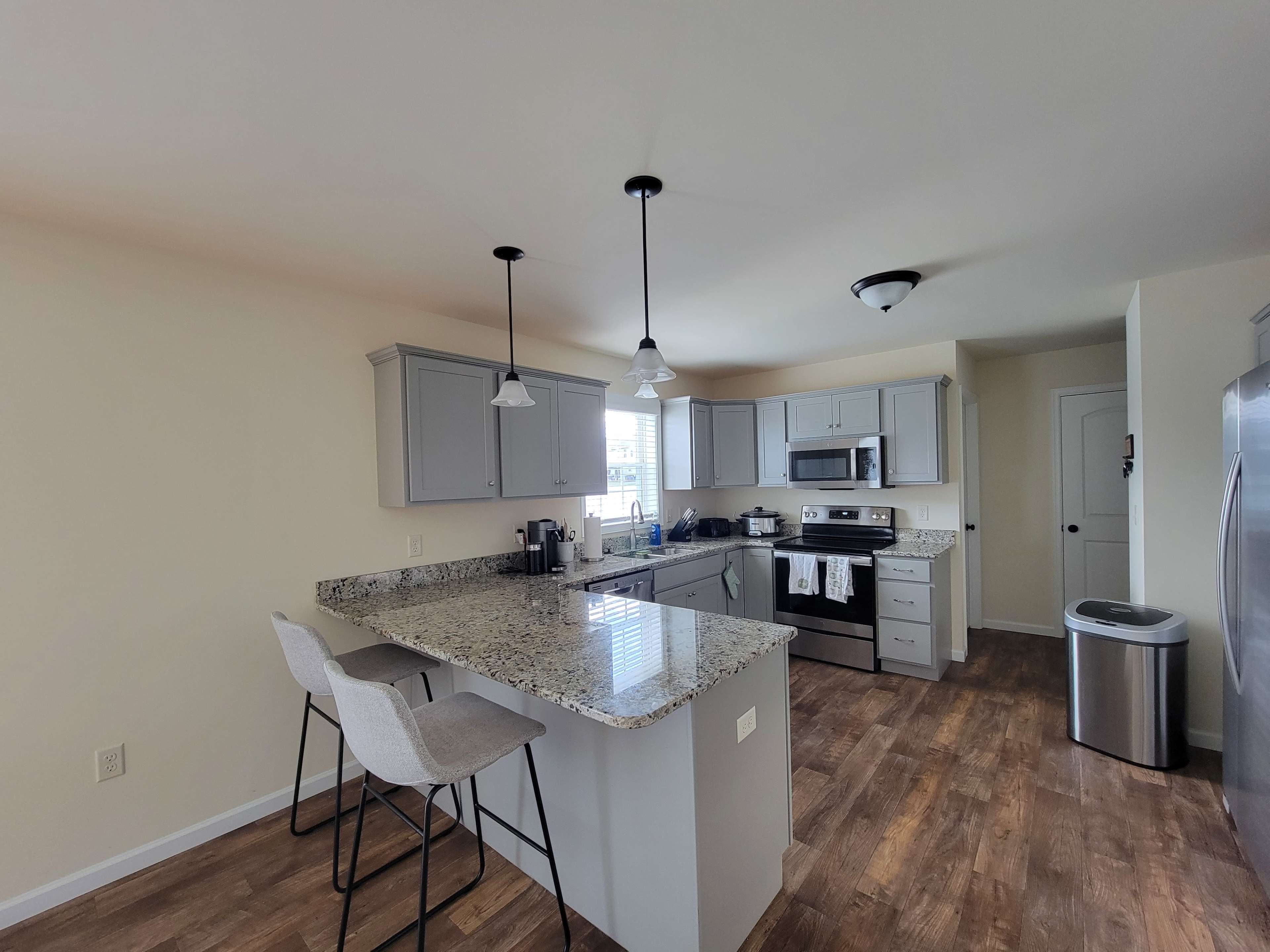 A modern kitchen with gray cabinets, a granite countertop, and stainless steel appliances.