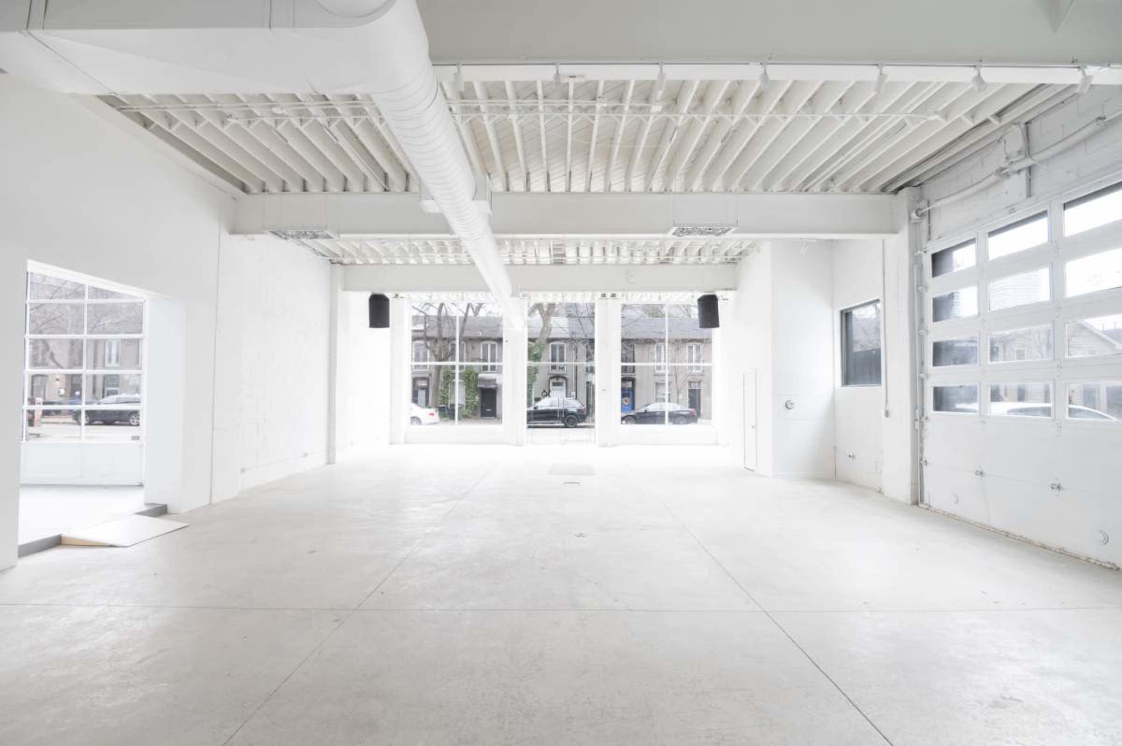 The image shows a large, empty industrial space with white walls and a concrete floor, featuring large windows along one side.