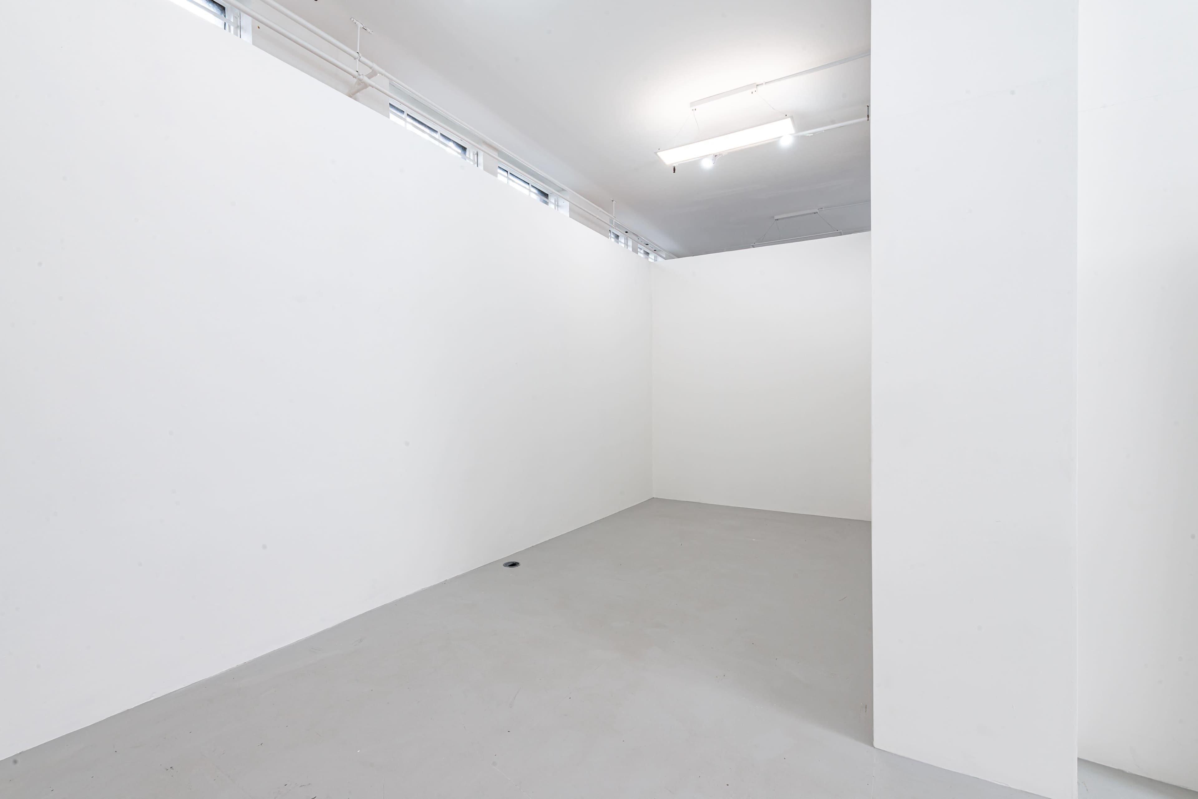 An empty, minimally lit room with plain white walls and a concrete floor.