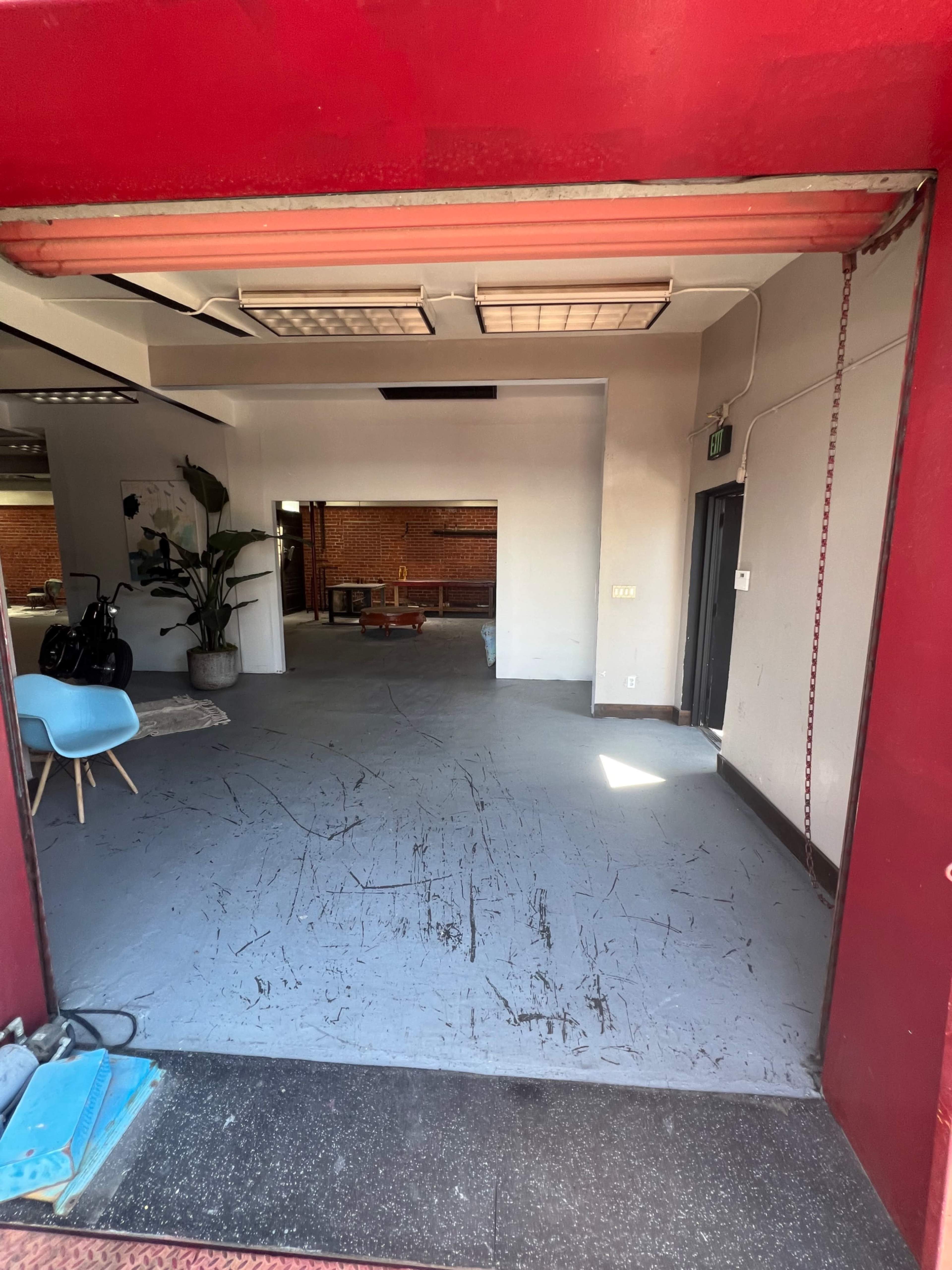 A large, open room viewed through a red entrance, featuring a smooth gray floor and minimal furnishings in a bright setting.
