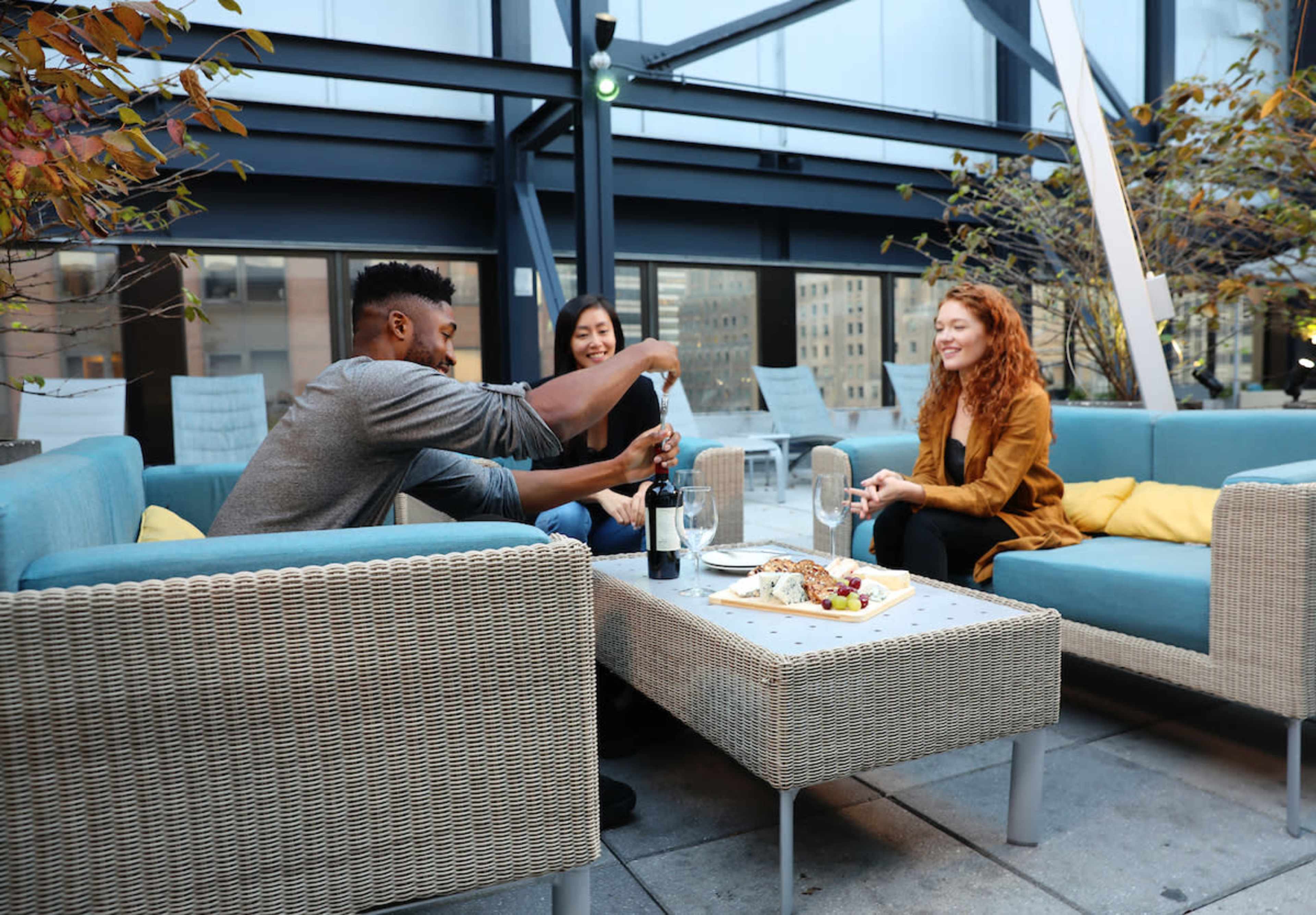 Three people are sitting on a patio, with a bottle of sparkling wine, and a platter of food on the table in front of them.