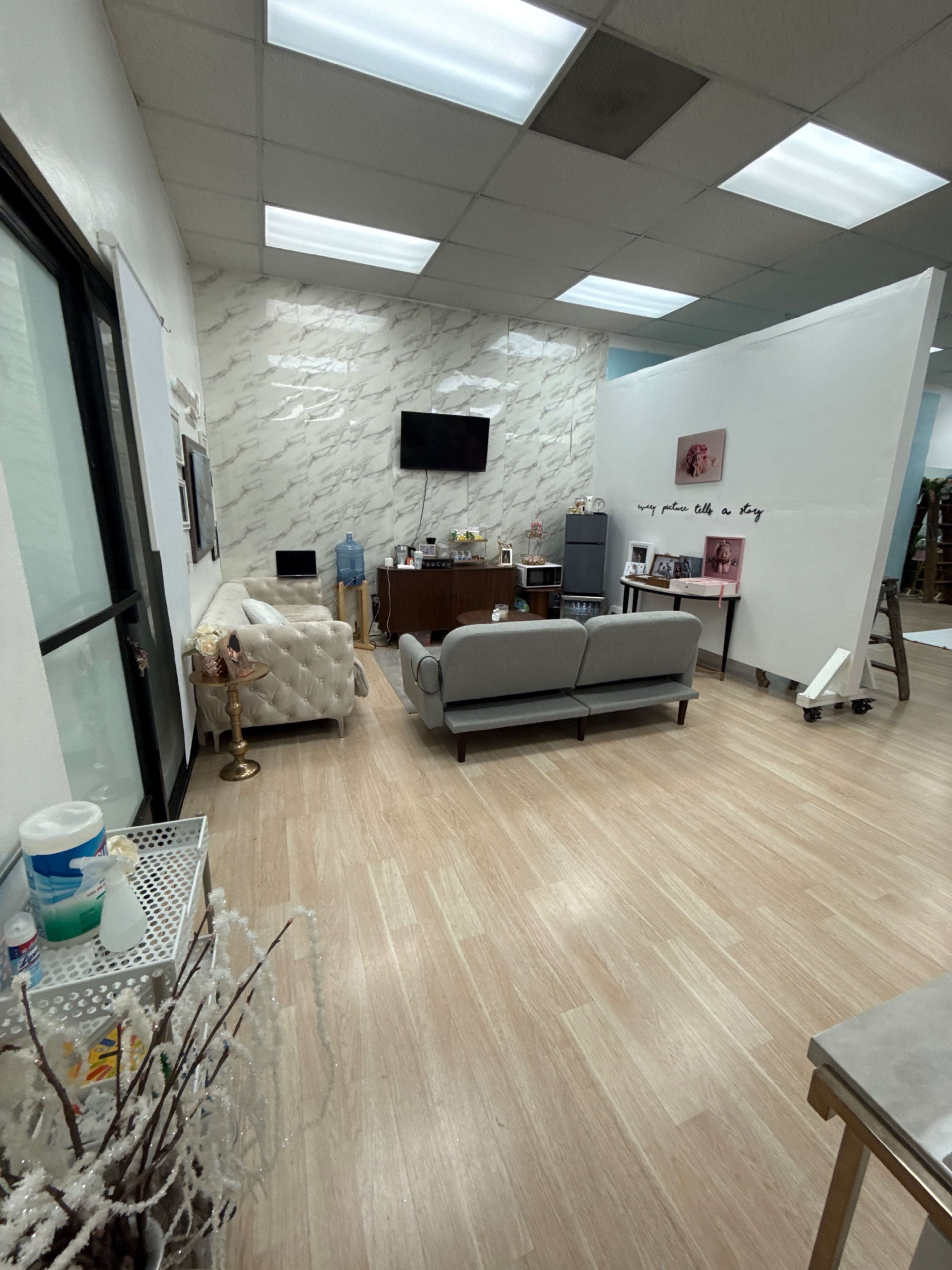 The image shows a bright, spacious reception area with a couch and several decorative elements, including a television and a styling station.