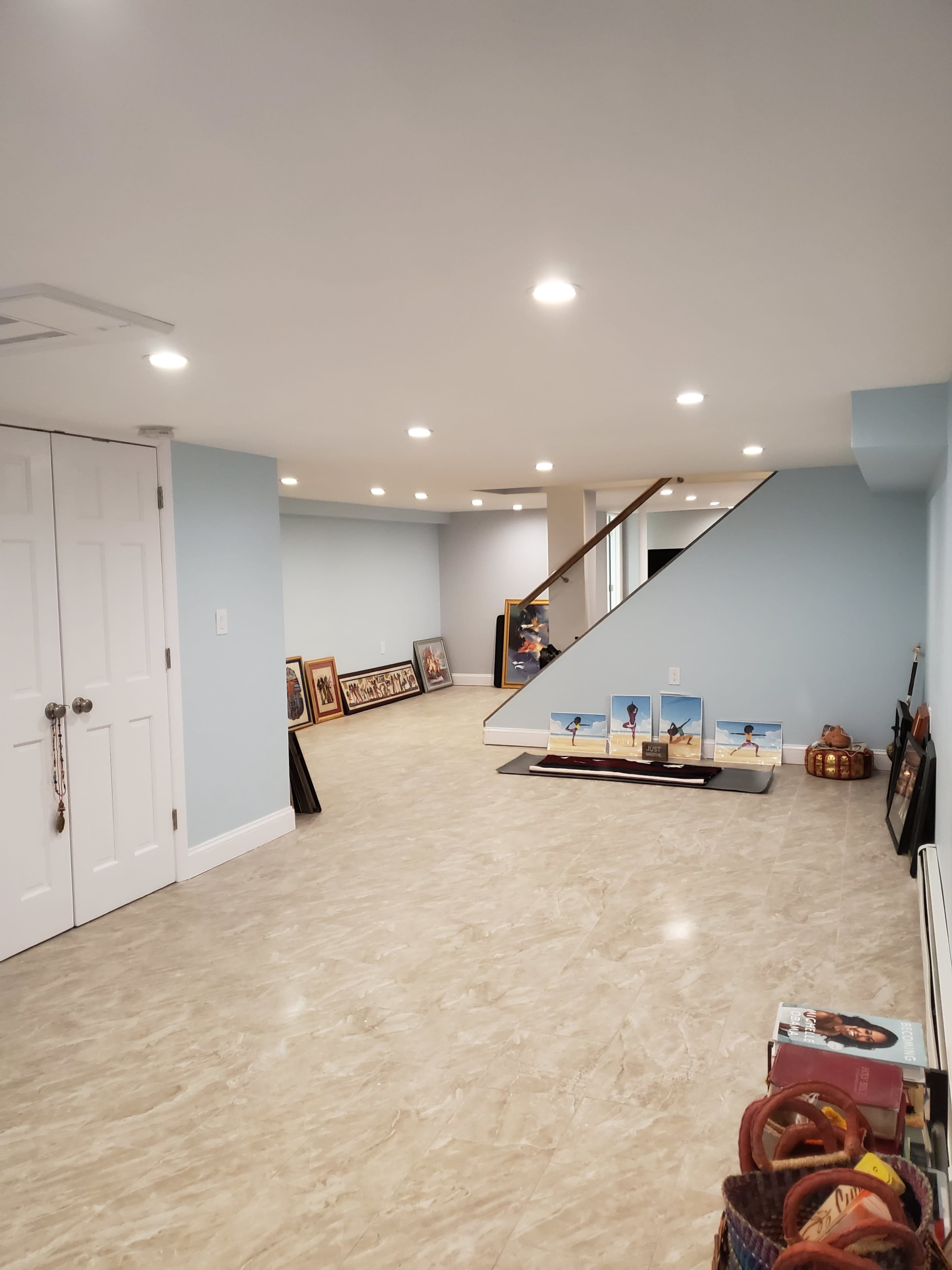 A spacious basement area with tiled flooring, light blue walls, and framed artwork leaning against the walls.