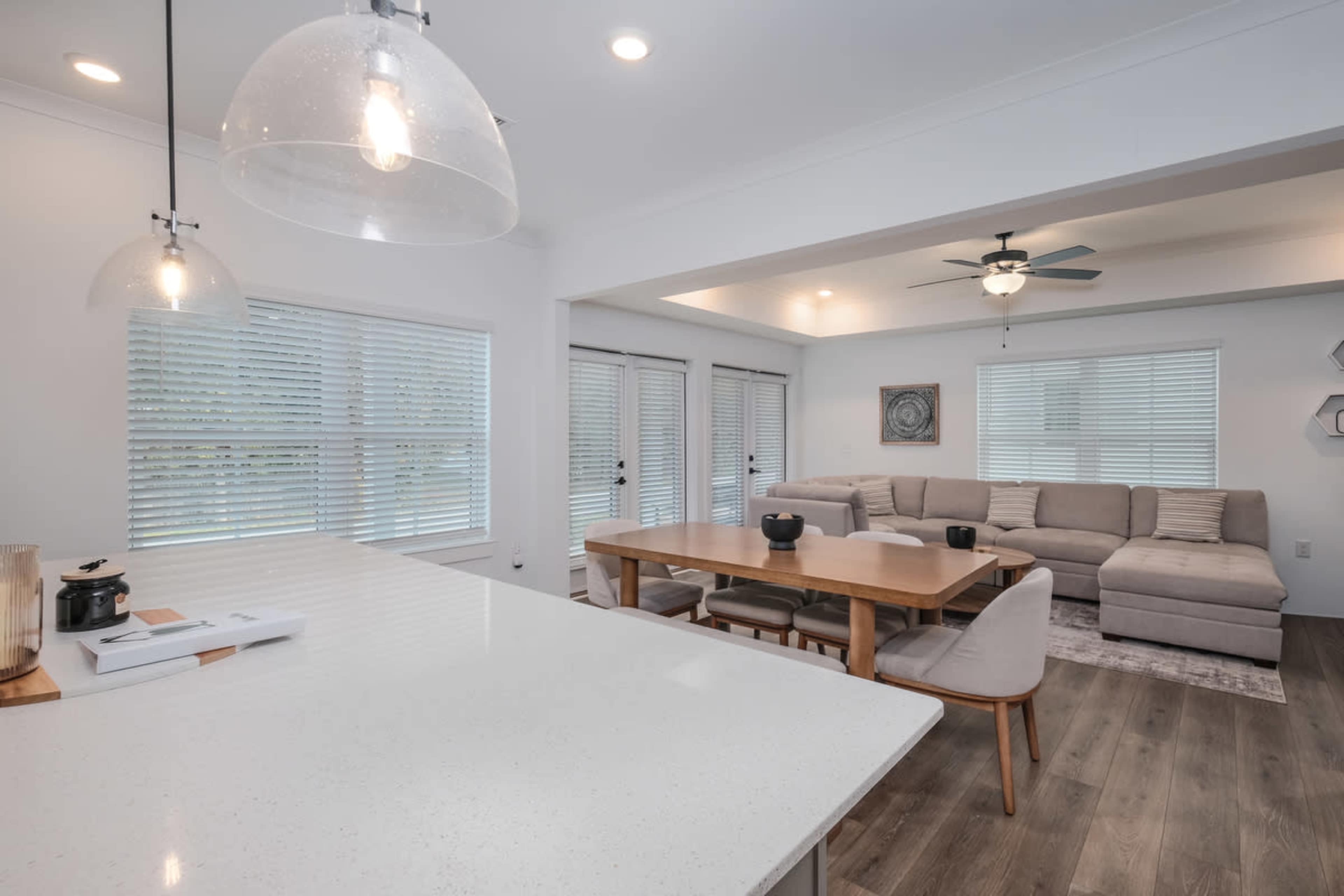 The image shows a modern open-concept living space featuring a kitchen with a large island and a dining area adjacent to a cozy living room with a sectional couch.