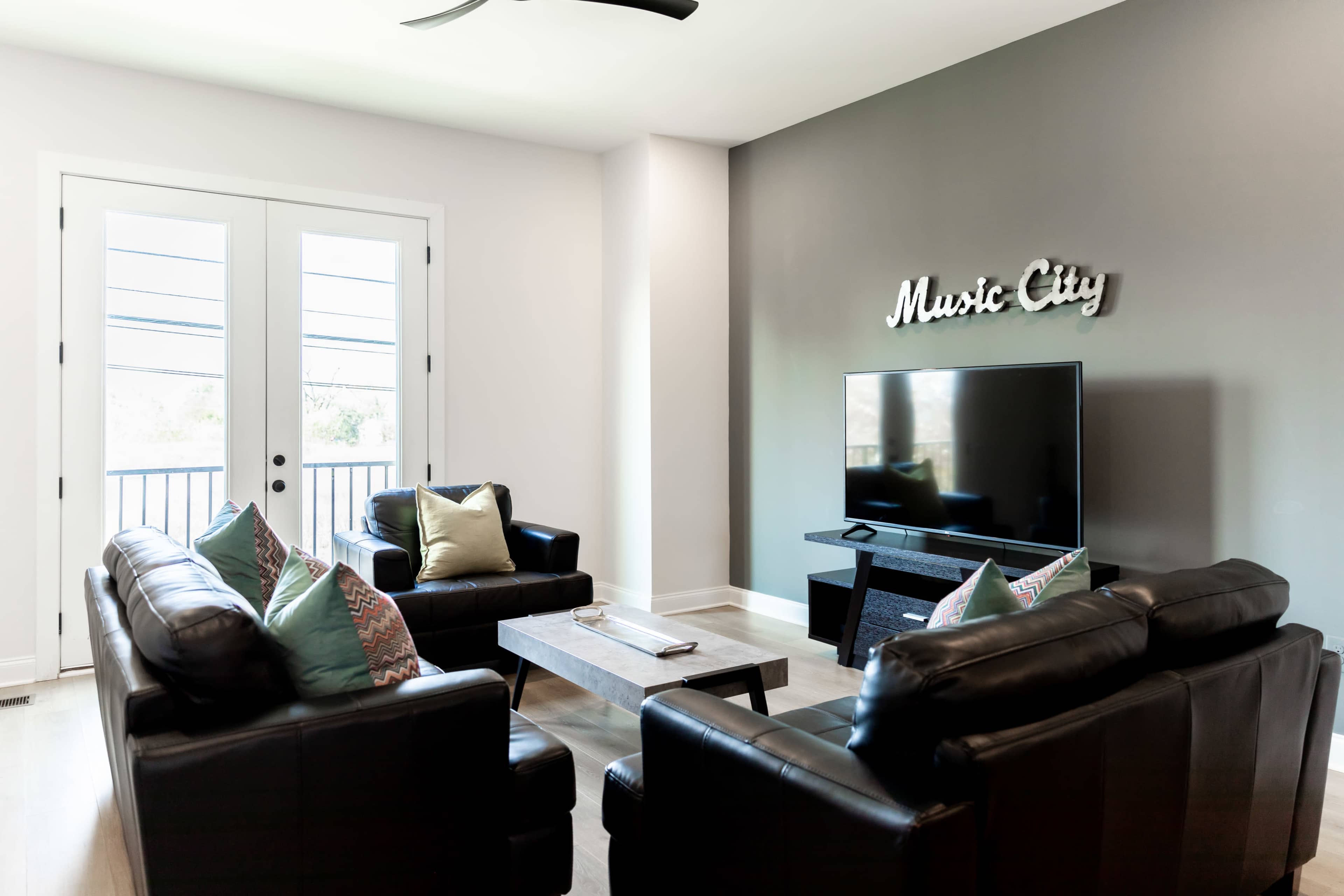 A modern living room features leather sofas, a television on a stand, and a "Music City" sign on the wall.