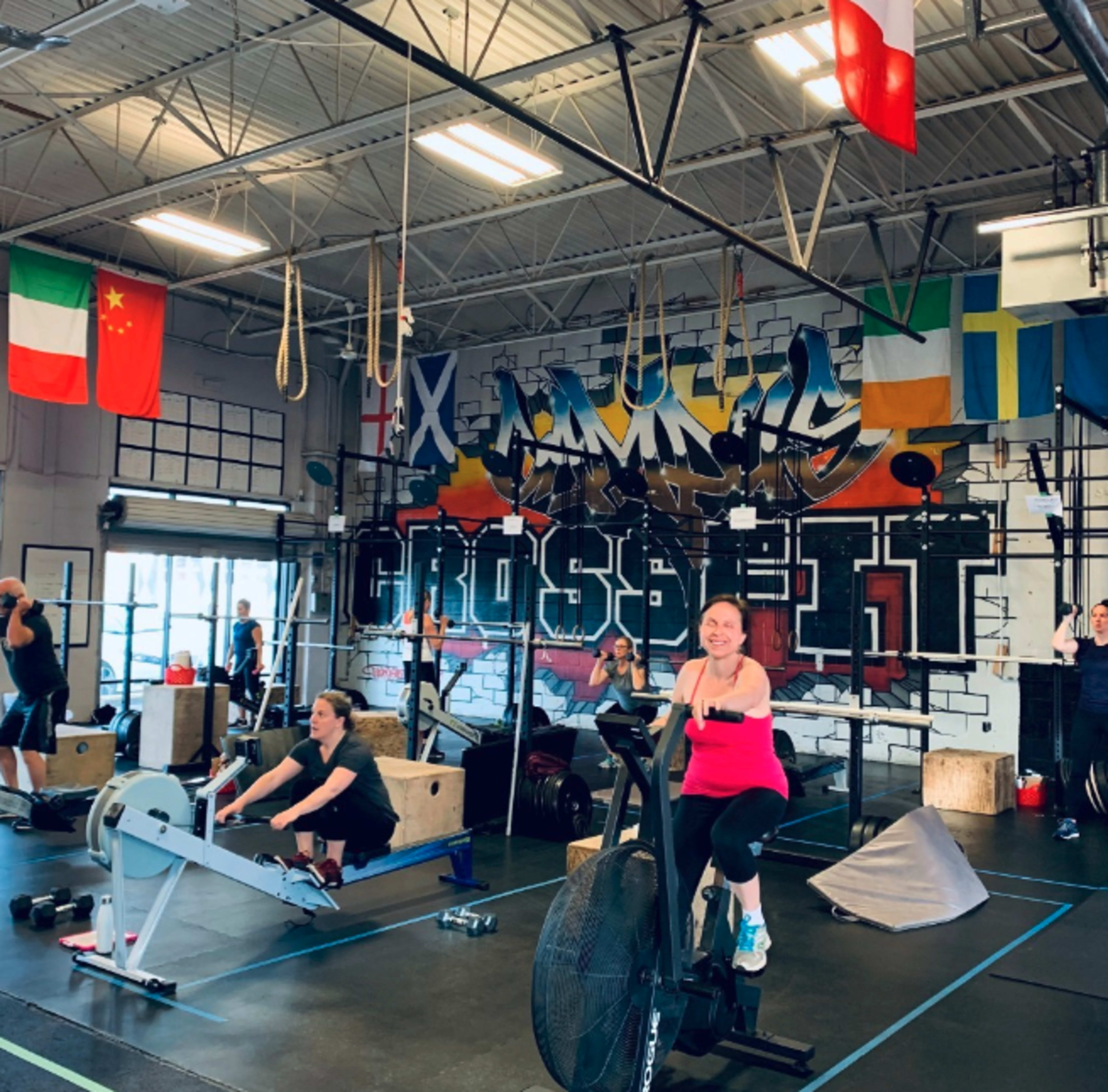 A group of people exercises in a gym adorned with various flags and a large "CROSSFIT" mural.