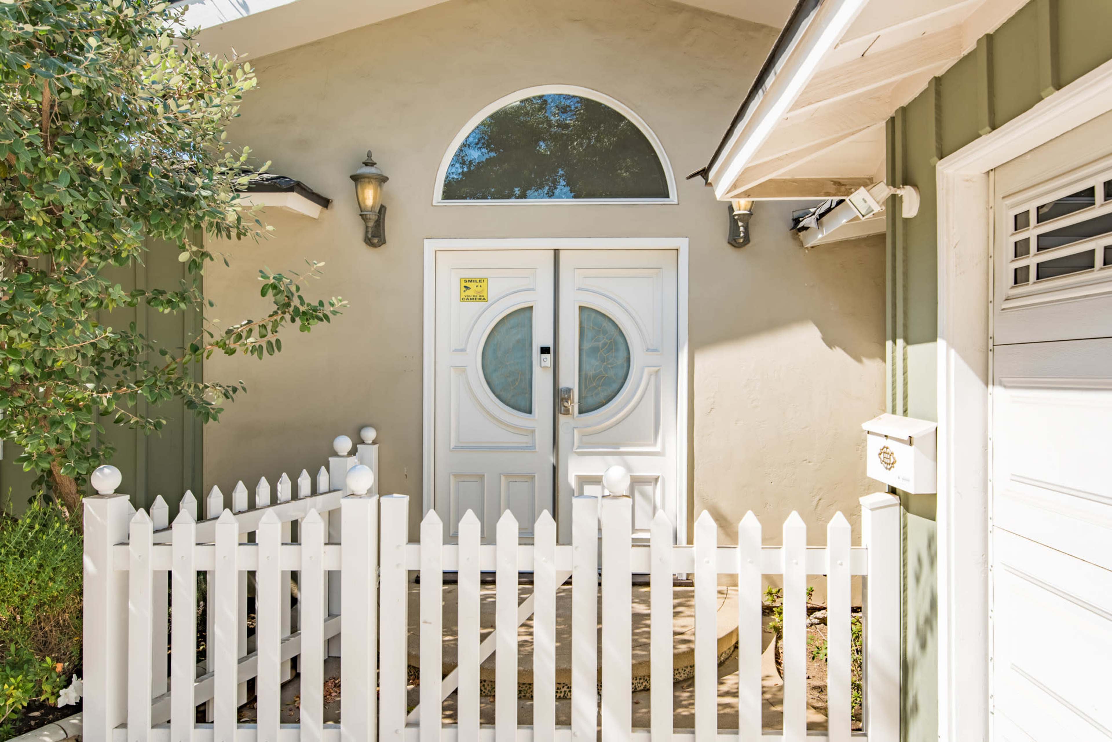 The image shows a white picket fence surrounding a front entrance featuring double doors with circular windows.