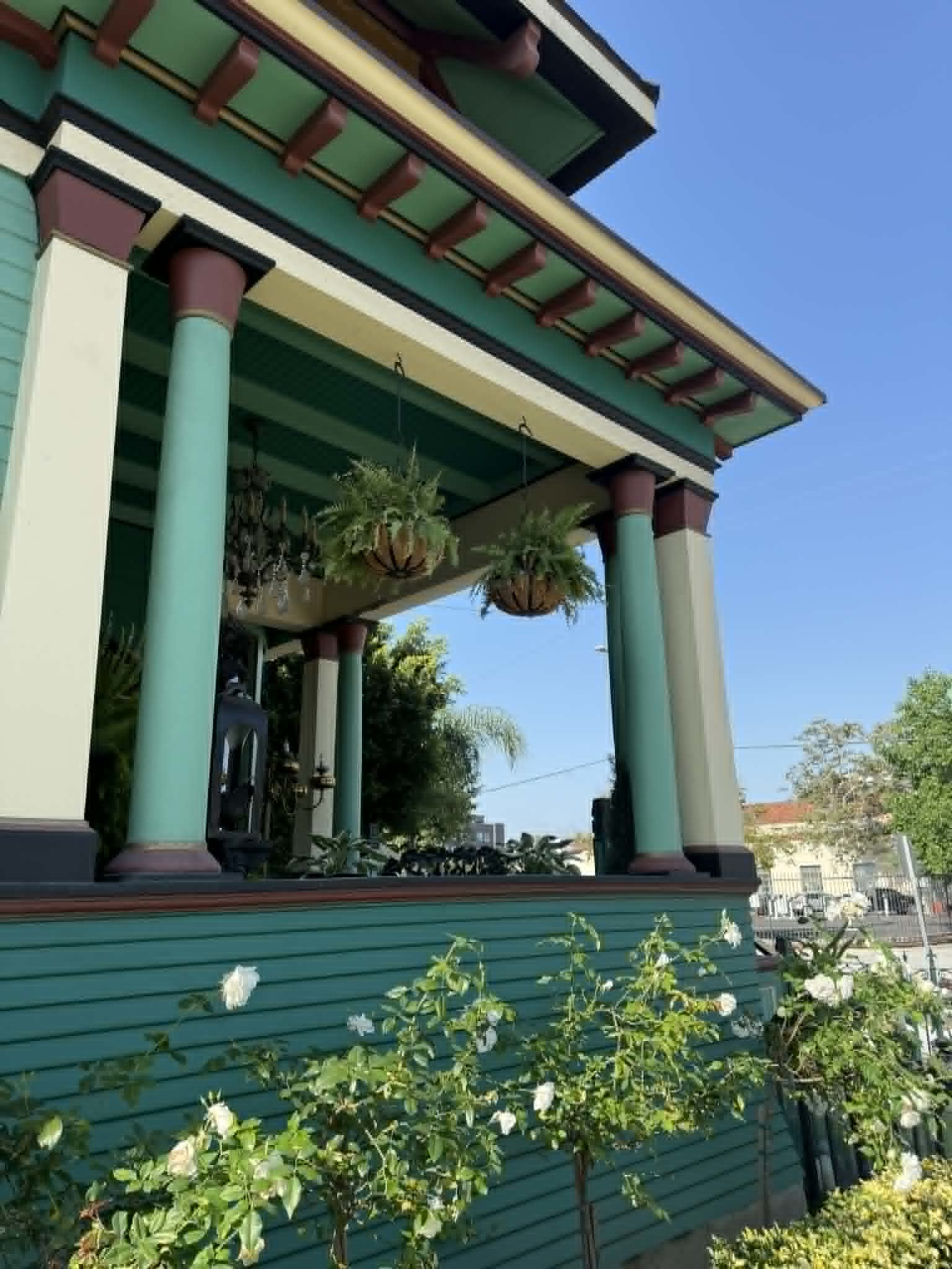 The image shows a colorful house with green siding, decorative columns, and hanging plants, set against a clear blue sky.