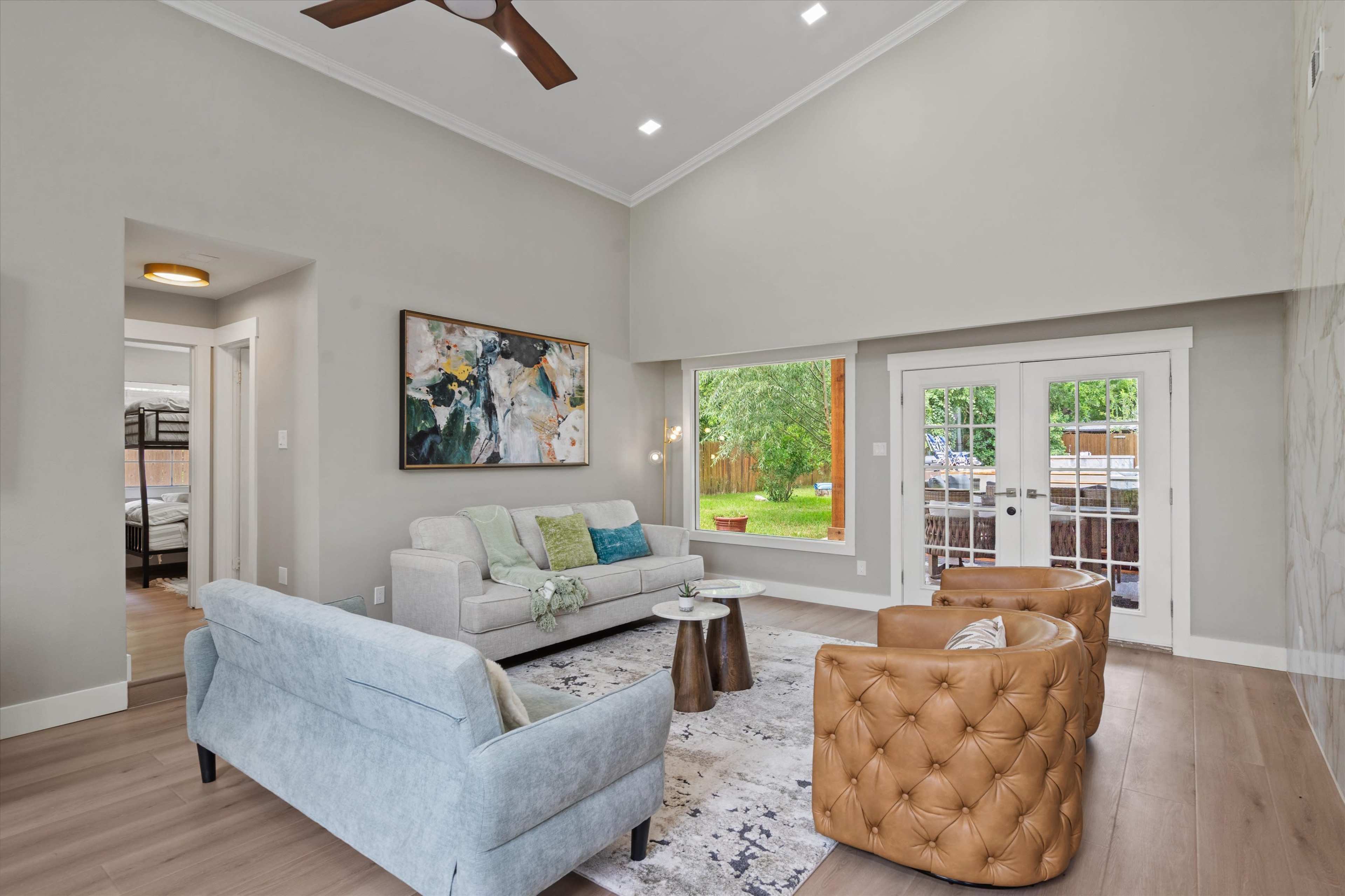 The living room features a light gray sofa, two brown leather armchairs, and a large window overlooking a backyard.