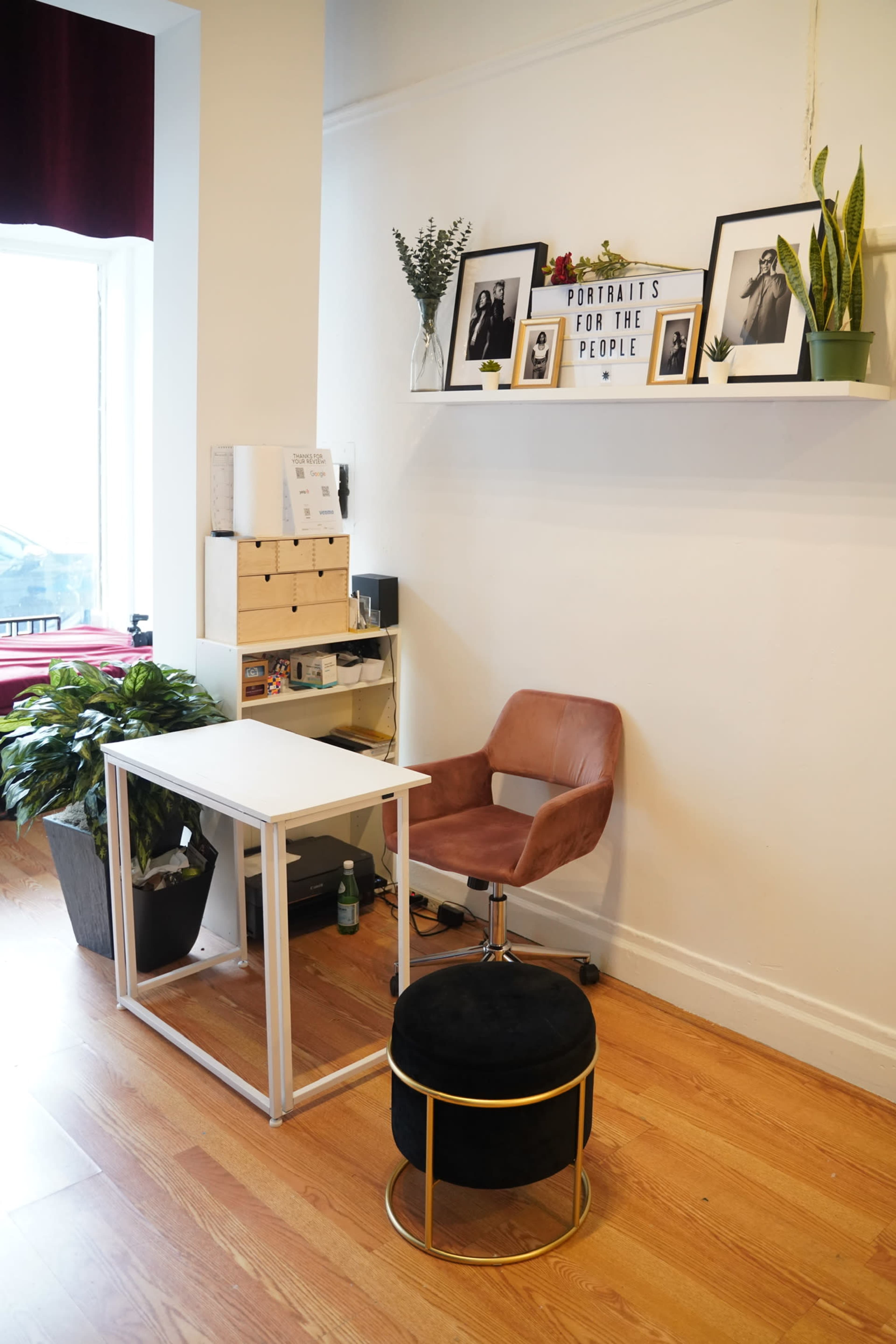 A small workspace featuring a white desk, a brown chair, and a shelf with framed photographs and plants.