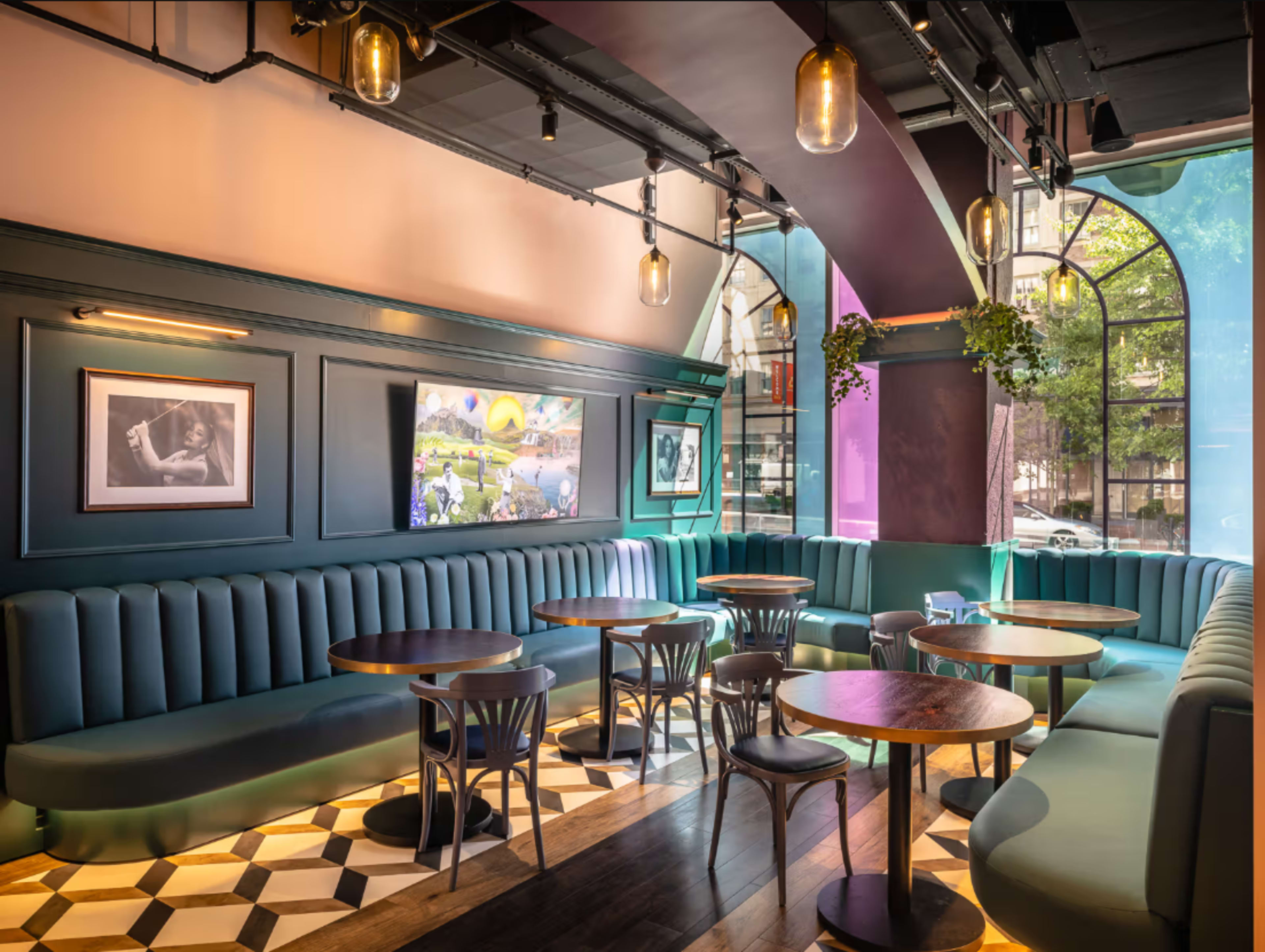 The image shows a modern cafe interior with curved seating, wooden tables, and large windows allowing natural light to enter.