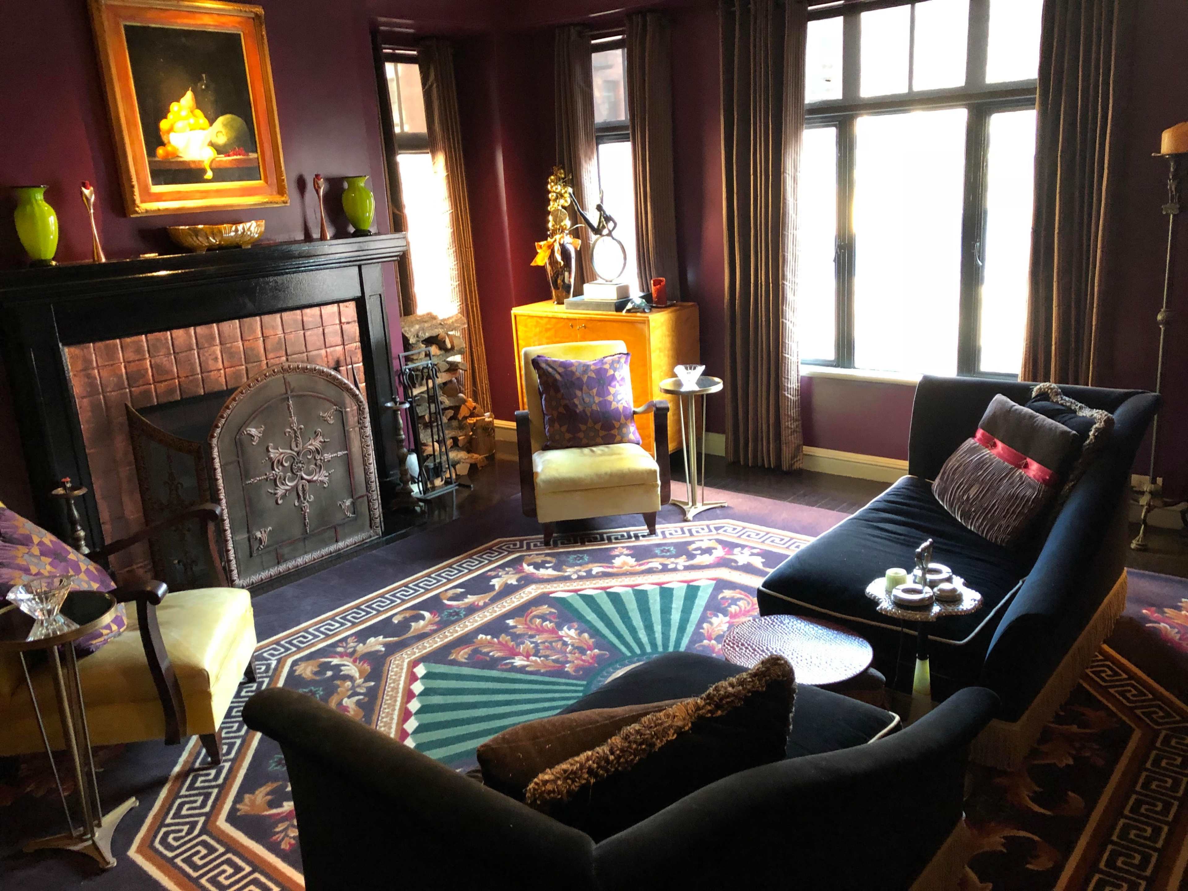 The room features a darkly painted interior with a fireplace, two armchairs, a black sofa, and a decorative rug.