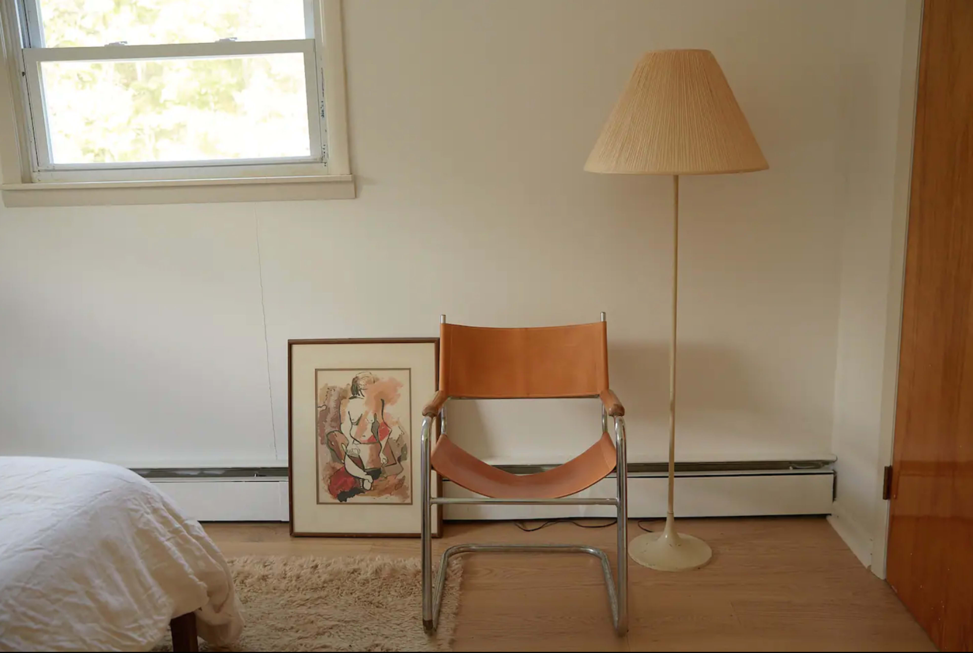 A wooden floor features a chair and a floor lamp beside a framed artwork against a white wall.
