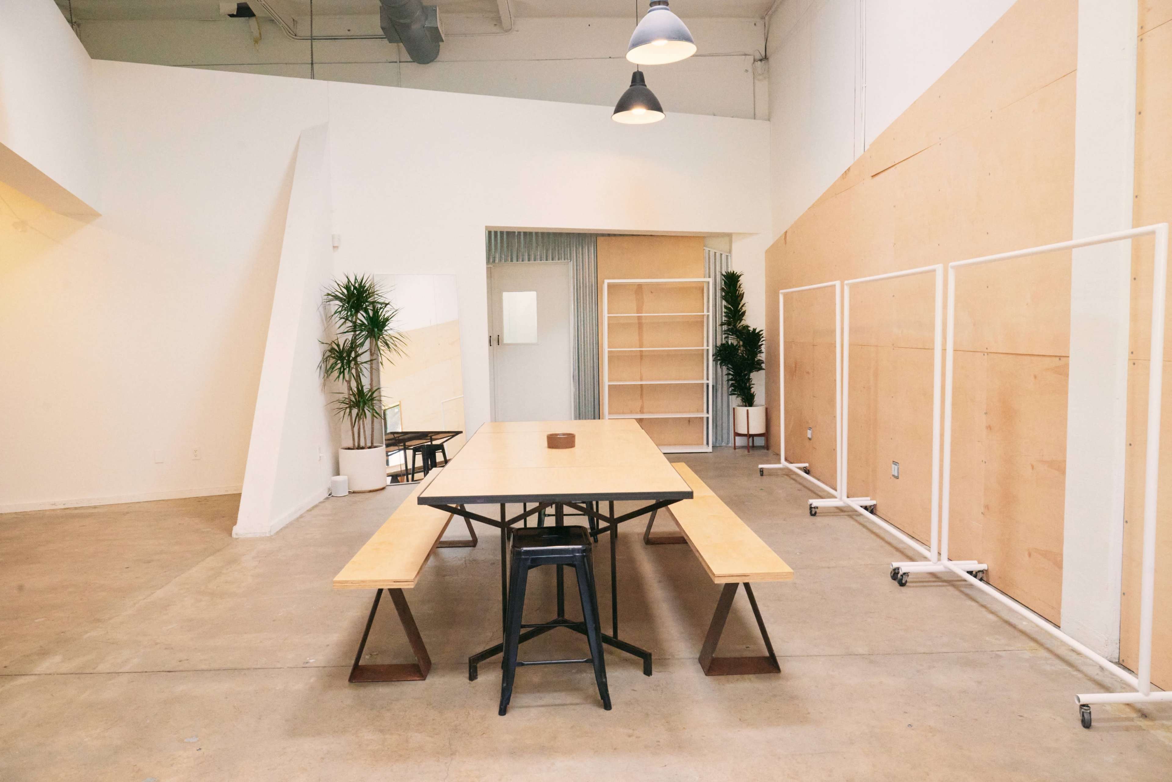 A spacious, modern room with a long wooden table and benches, surrounded by minimalistic decor and plants.