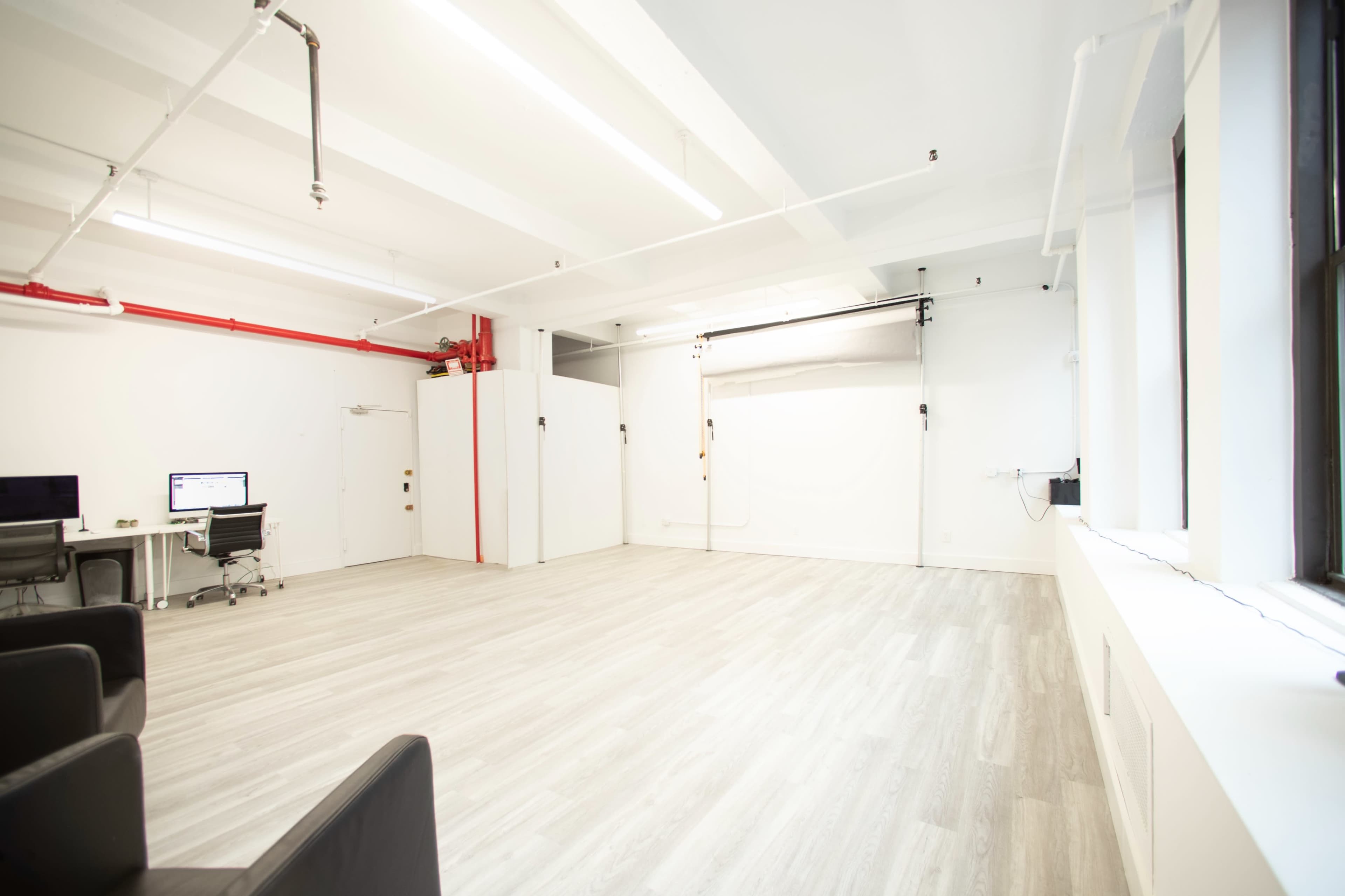 A bright, uncluttered studio space with light-colored flooring and a backdrop setup for photography in one corner.