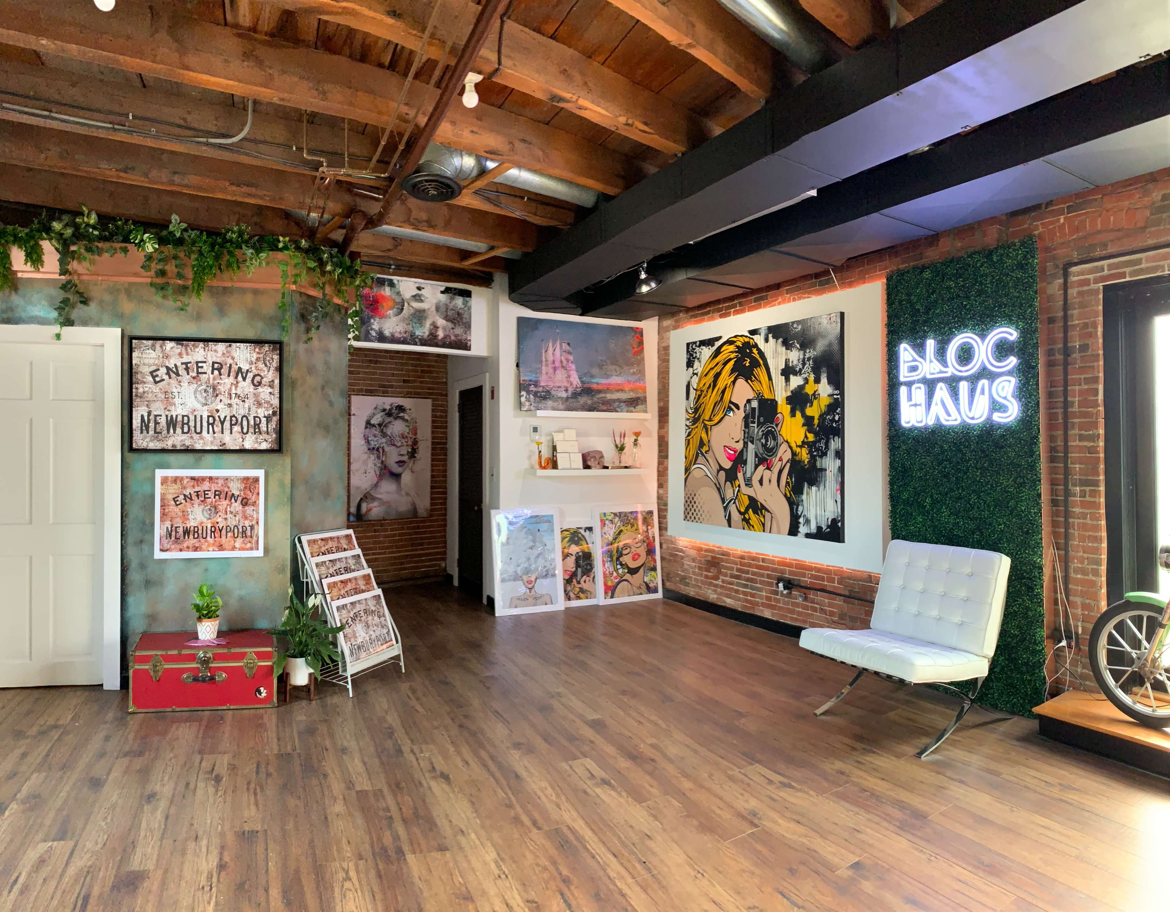 The interior of a creative space features exposed wood beams, brick walls adorned with various artworks, and a bright green wall displaying the name "BLOC HAUS."