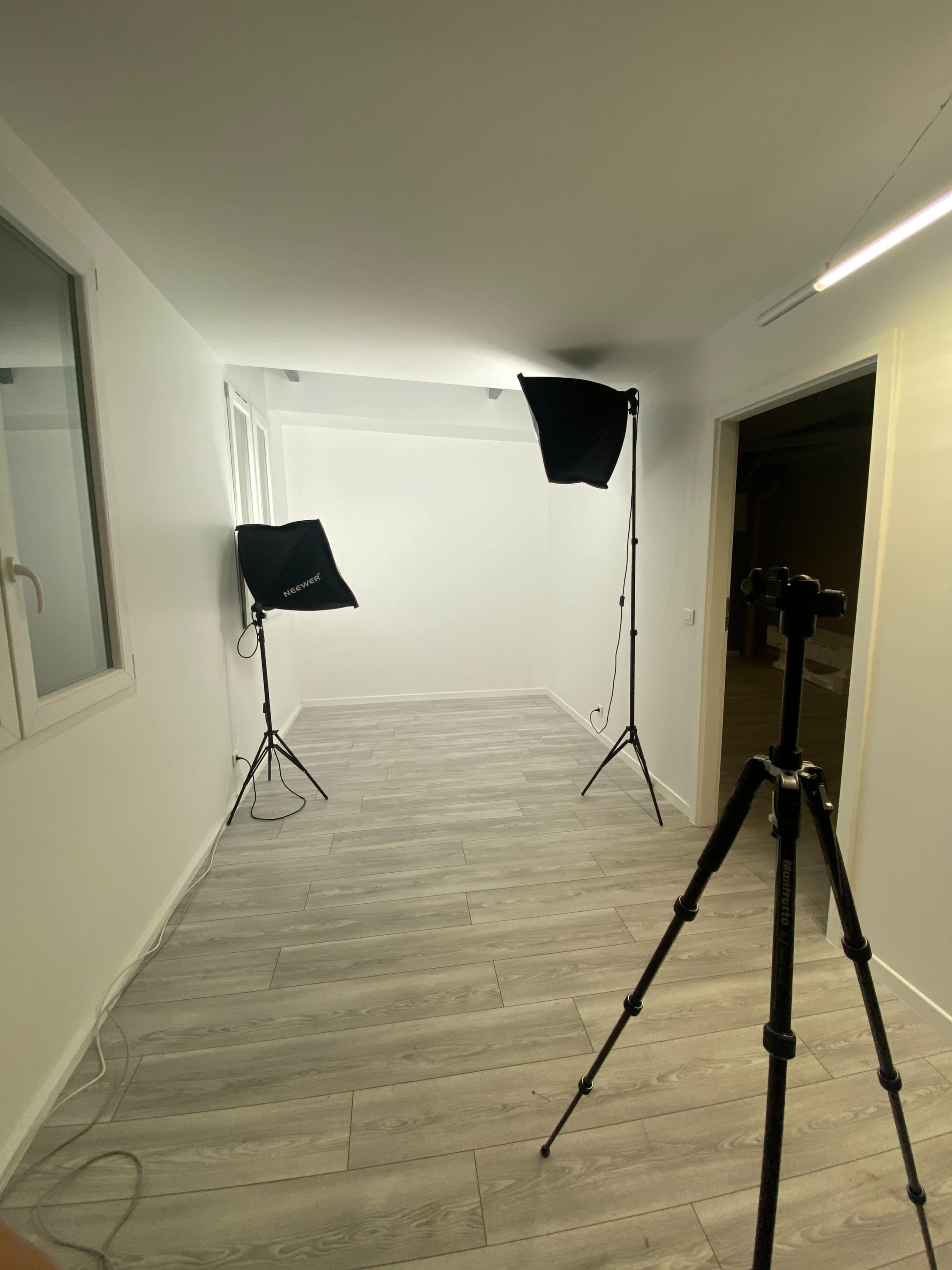 The image shows a well-lit, empty room with two photography lights on stands and a tripod set up in the corner.