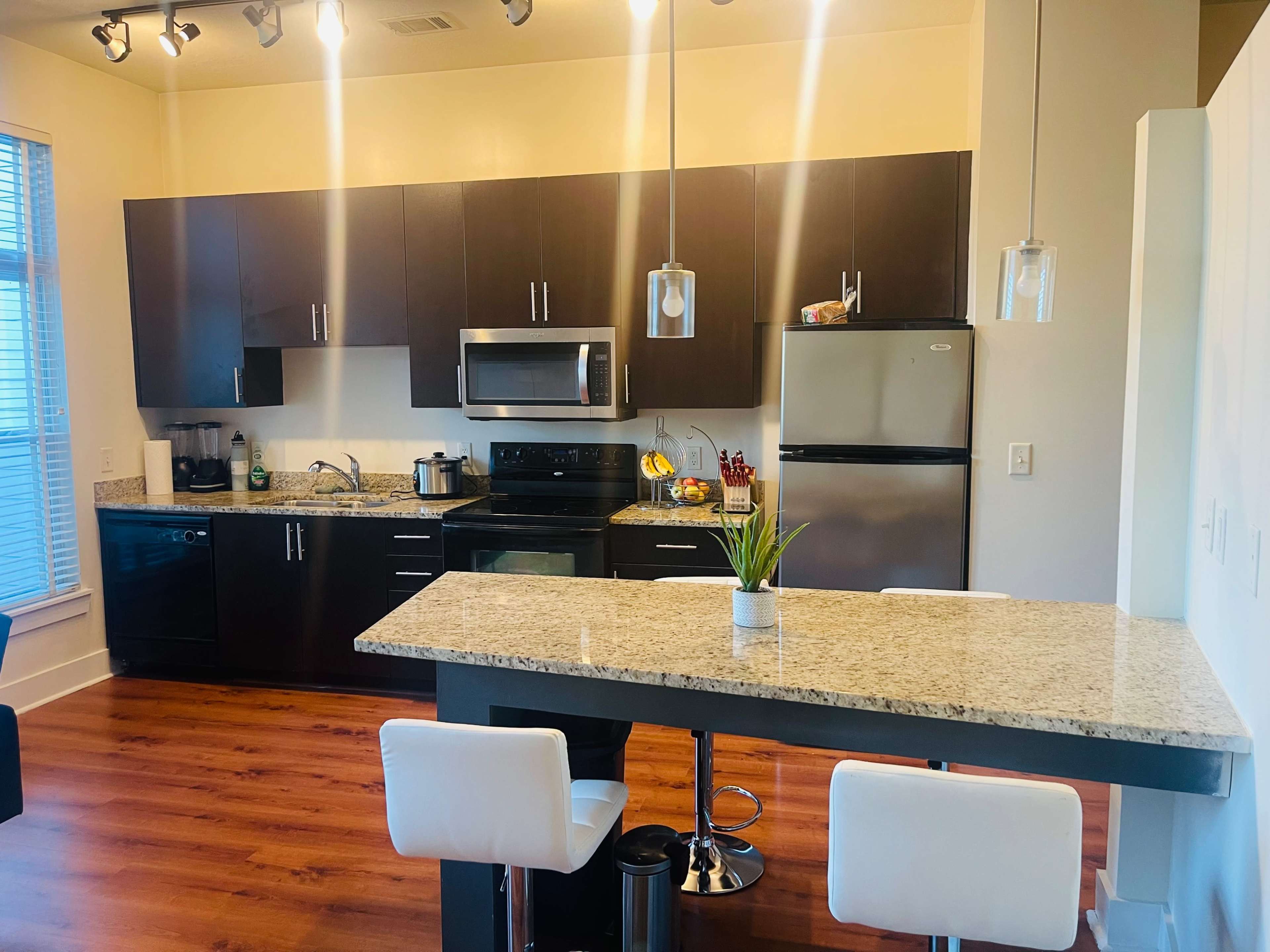 A modern kitchen with dark cabinets, stainless steel appliances, and a granite countertop with two stools.