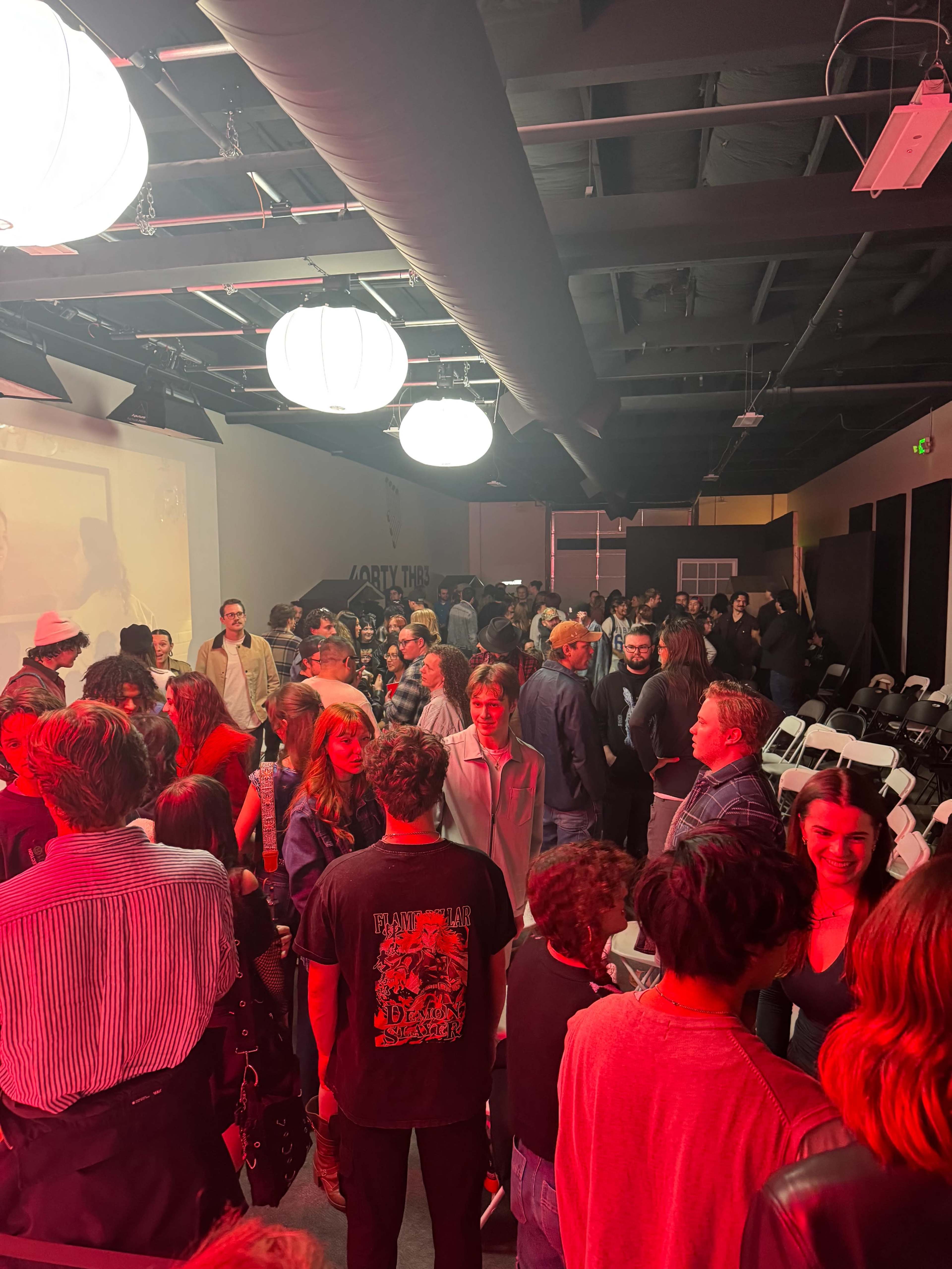 A crowded indoor space shows a diverse group of people gathered, with illuminated lanterns hanging from the ceiling.