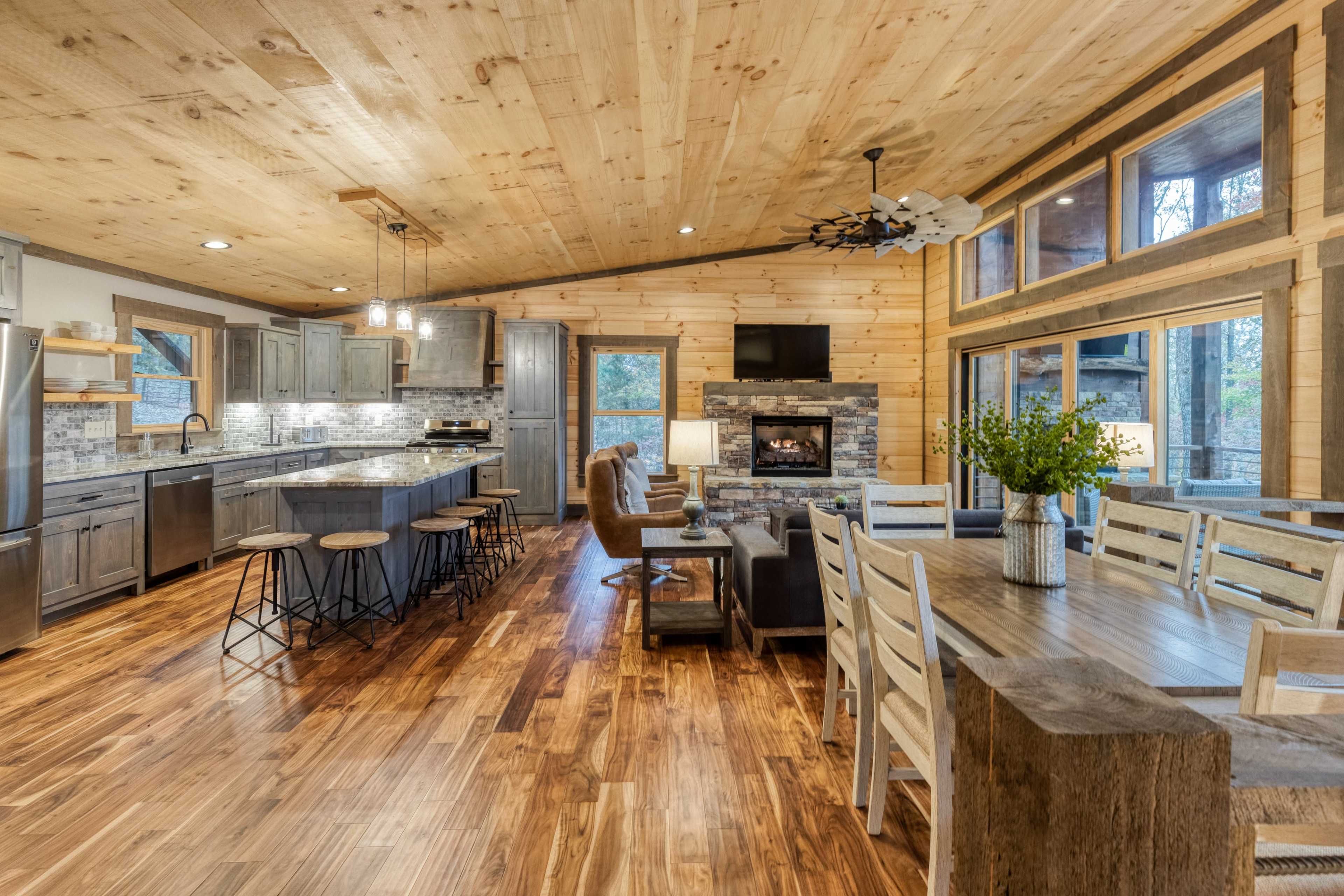A modern, open-concept kitchen and dining area in a cabin-style interior with wooden walls and flooring.