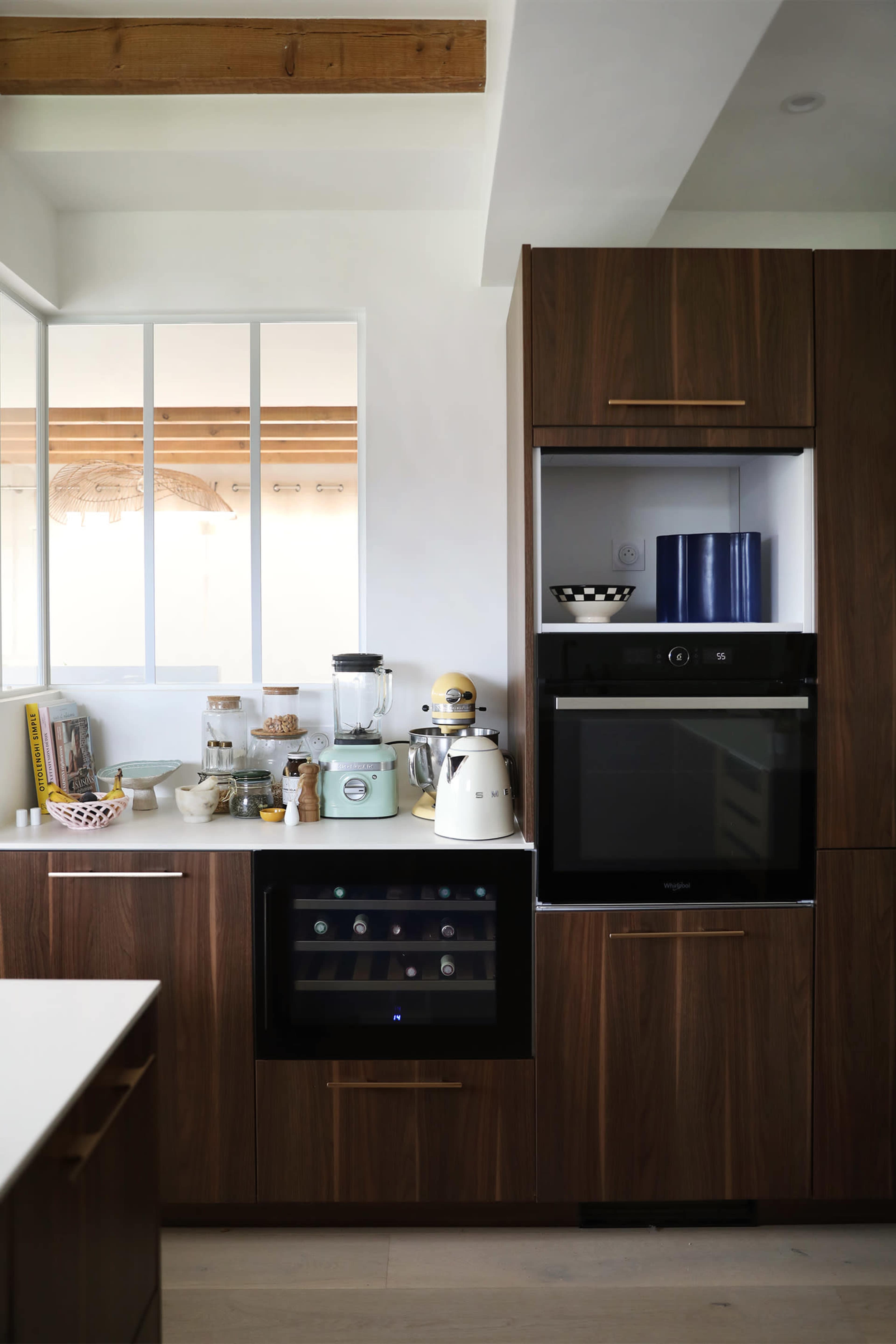 A modern kitchen with dark wood cabinetry, featuring an integrated refrigerator, a wine cooler, and various kitchen appliances on the countertop.