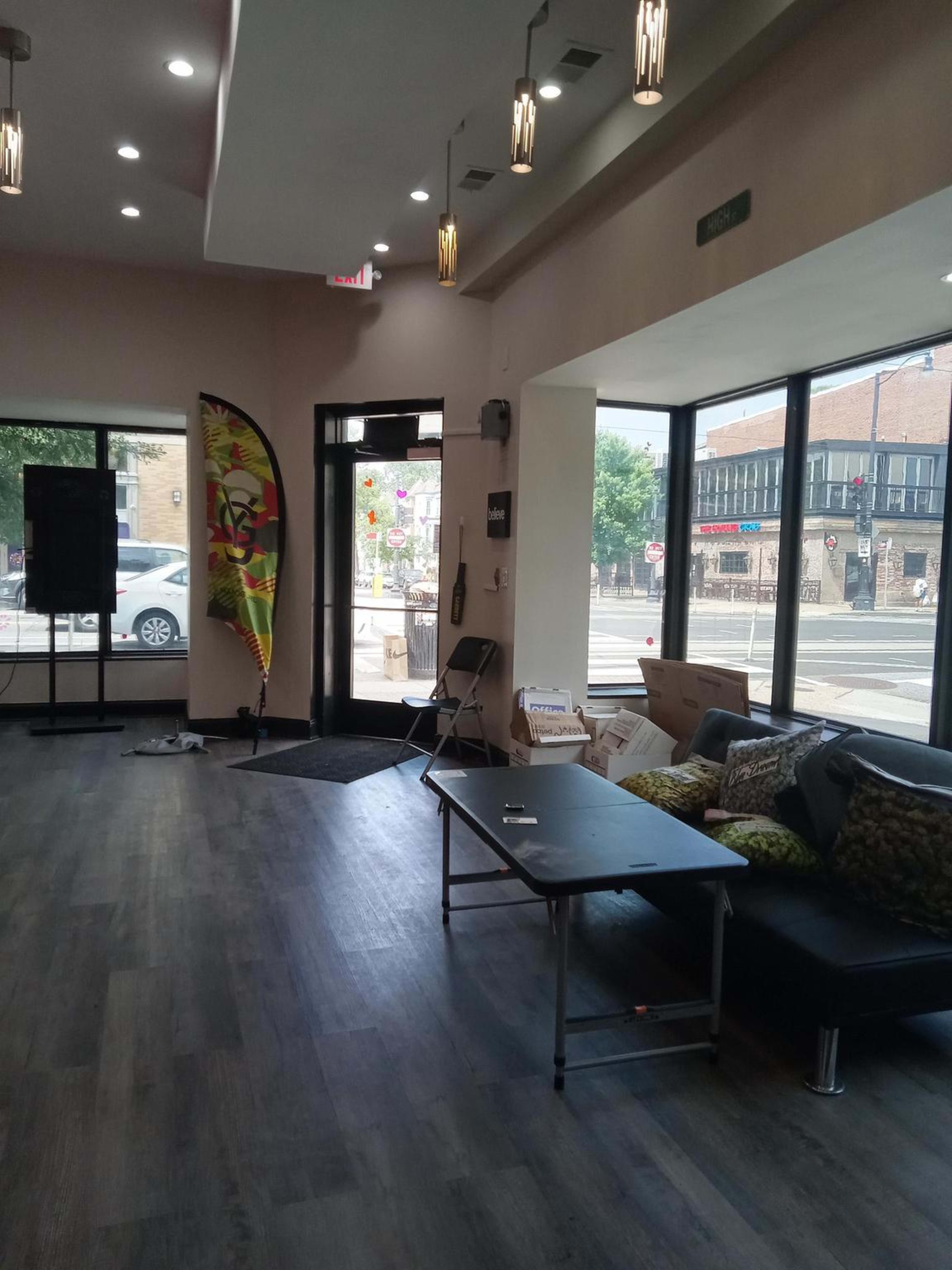 The image shows the interior of a spacious room with large windows, a small table, a chair, and a brightly colored flag near the entrance.