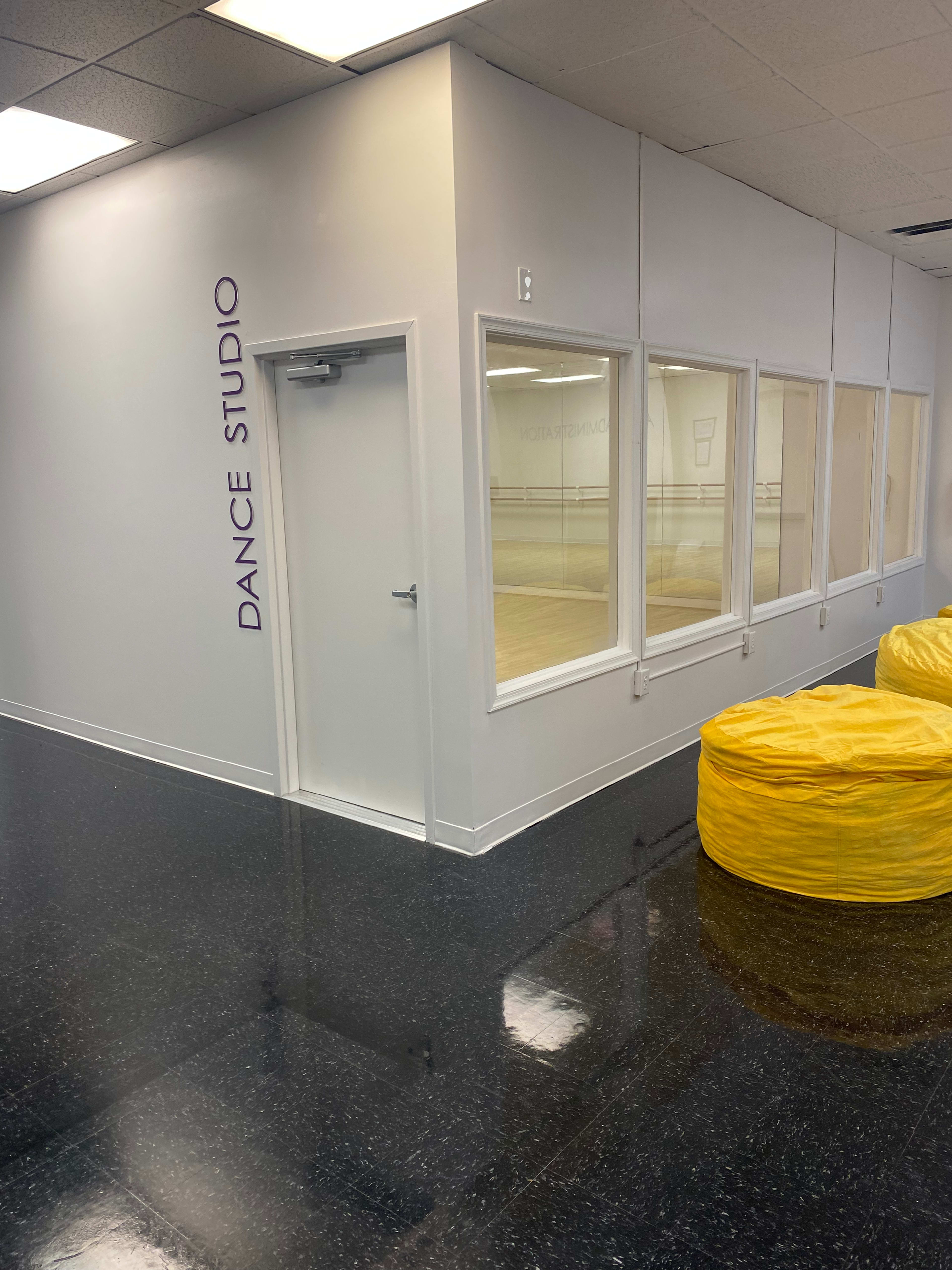 A dance studio entrance with a large window, bright yellow bean bags in front, and a polished black floor.