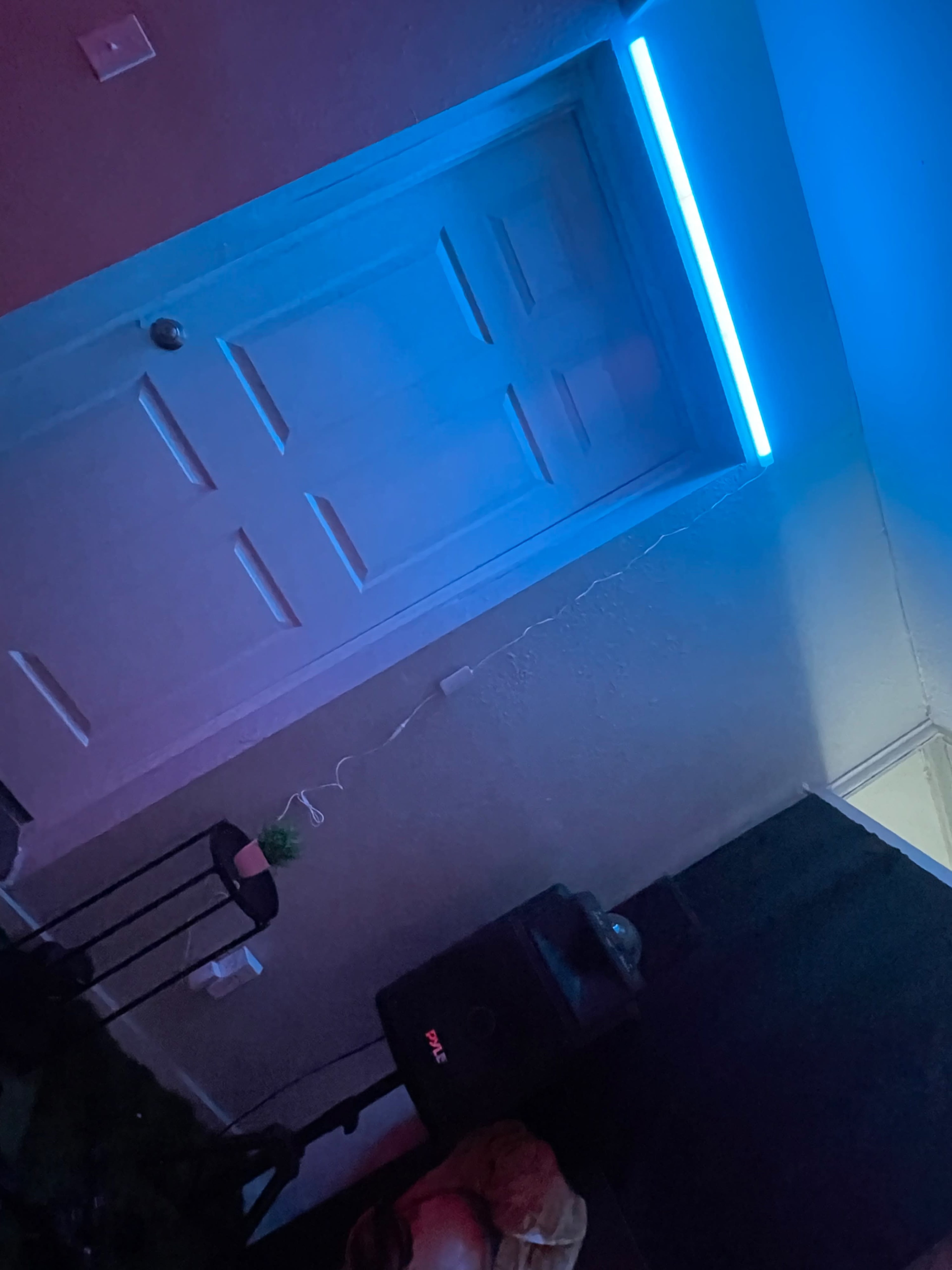 A dimly lit room features a closed door with a blue LED light above it and a small speaker nearby.