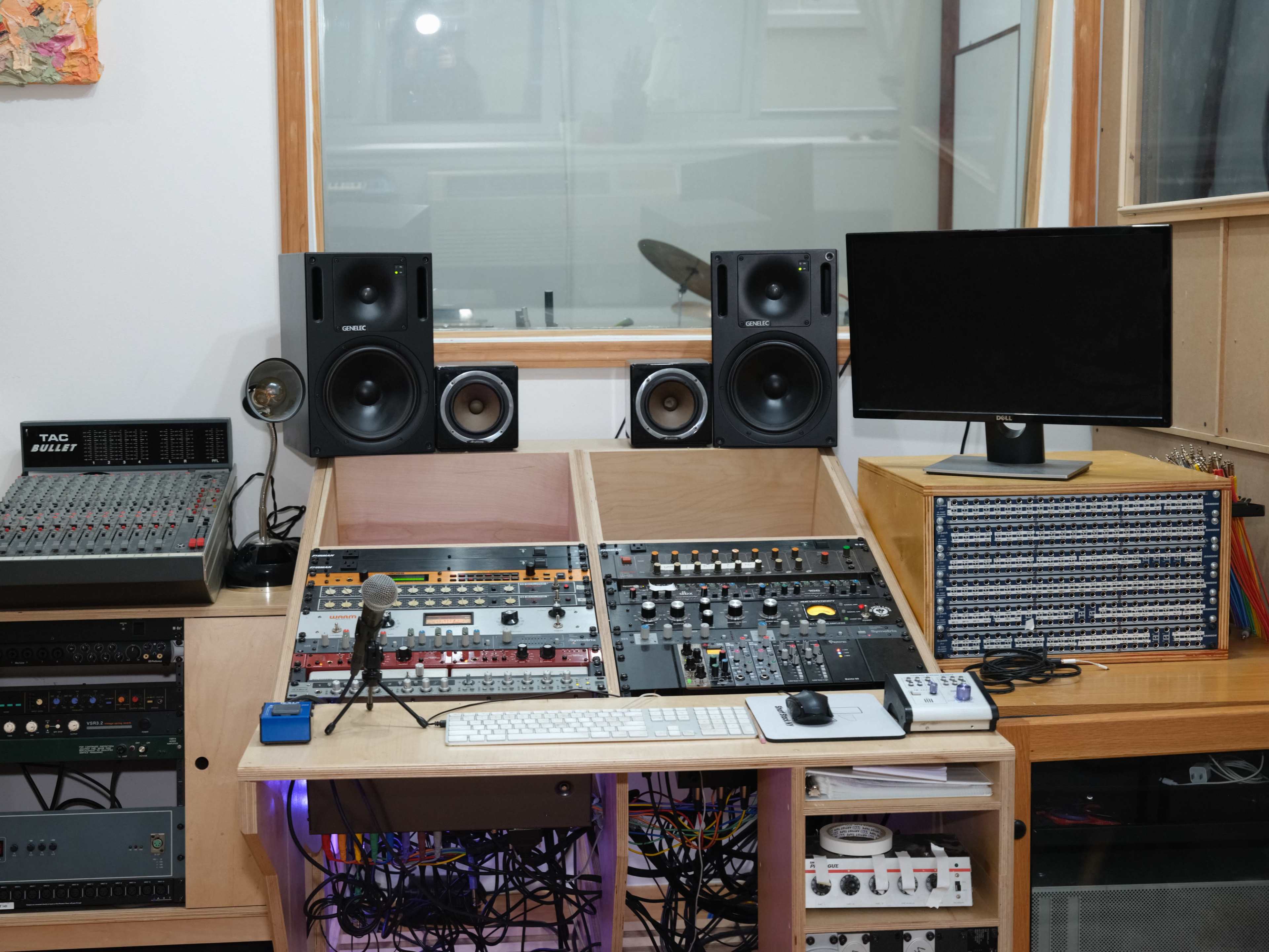 A recording studio desk is equipped with audio mixing equipment, speakers, a computer monitor, and various cables.