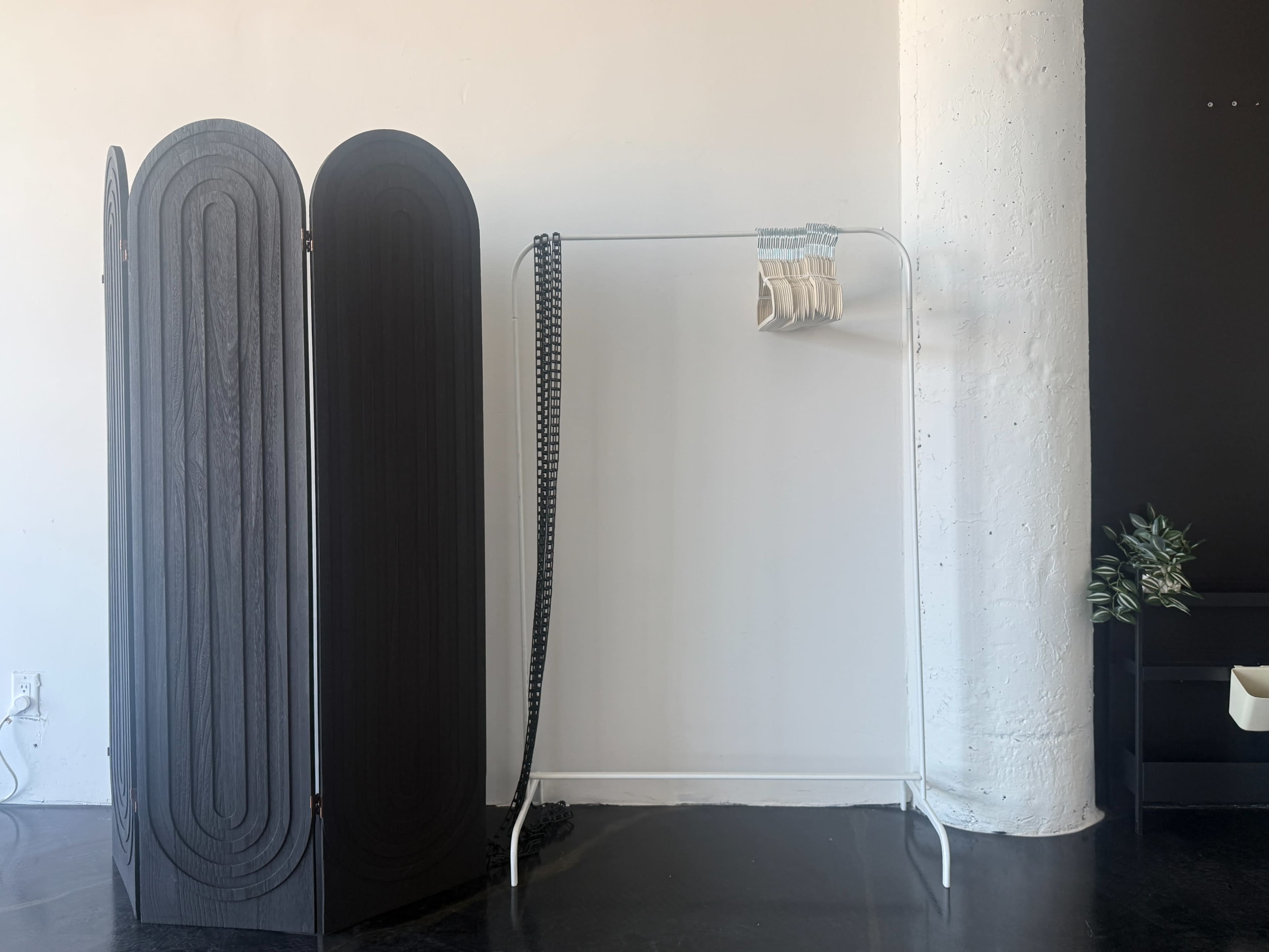 The image shows a minimalist room featuring a folding screen on the left and a clothes rack with hanging items on the right.