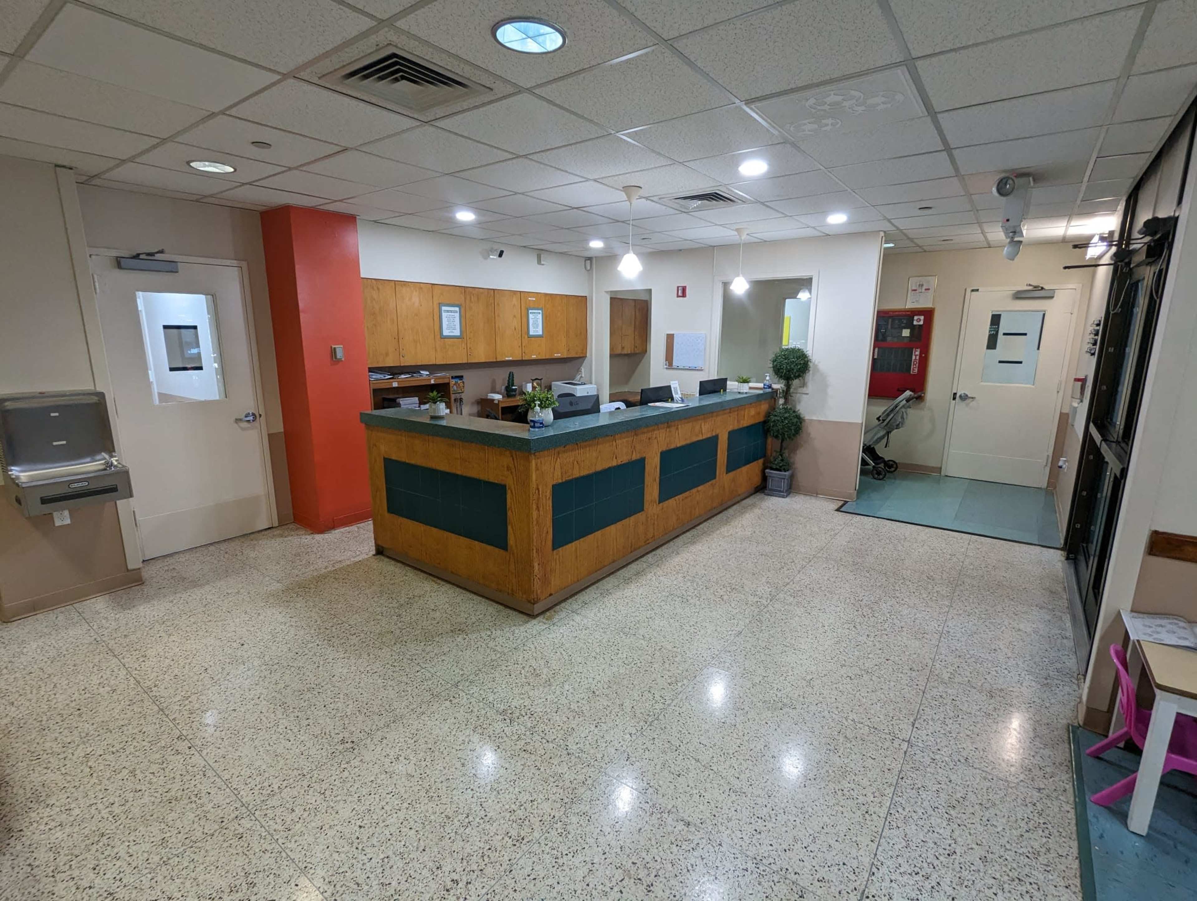 A reception area with a wooden front desk, a tiled floor, and various office equipment in a well-lit space.