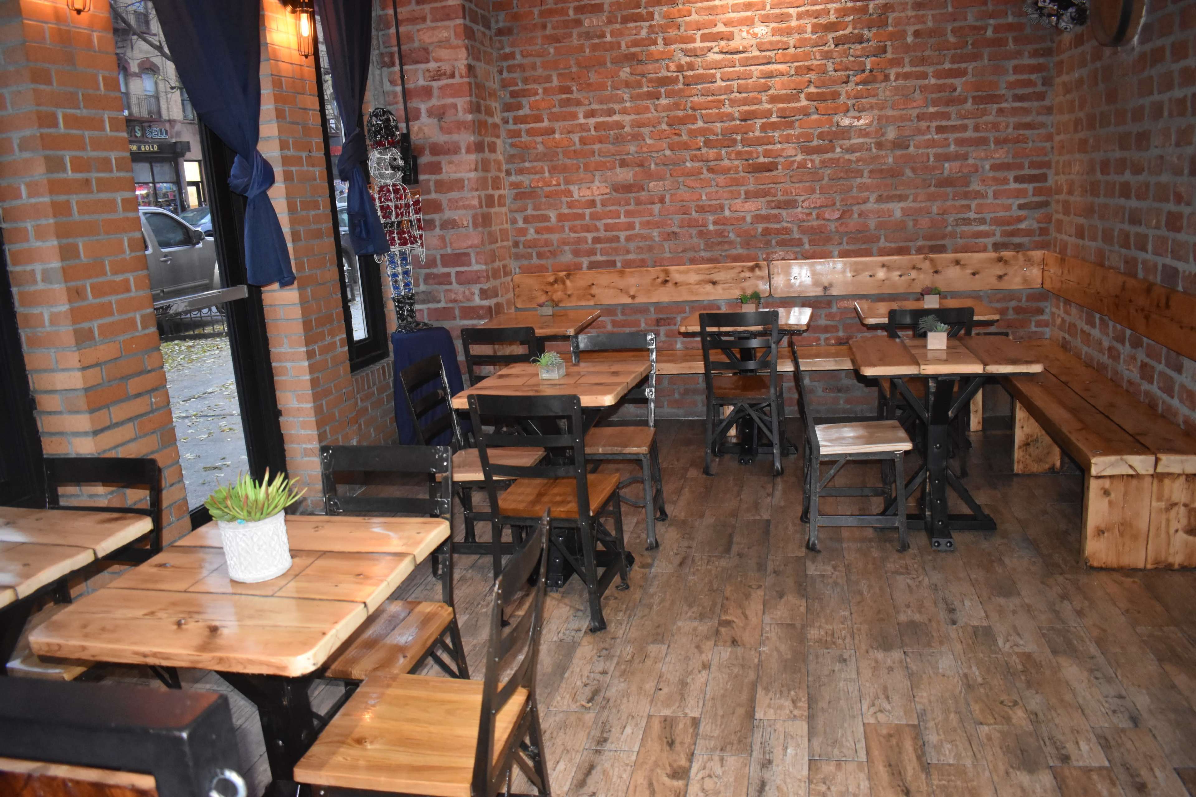 The image shows an empty restaurant interior with wooden tables and chairs against exposed brick walls.