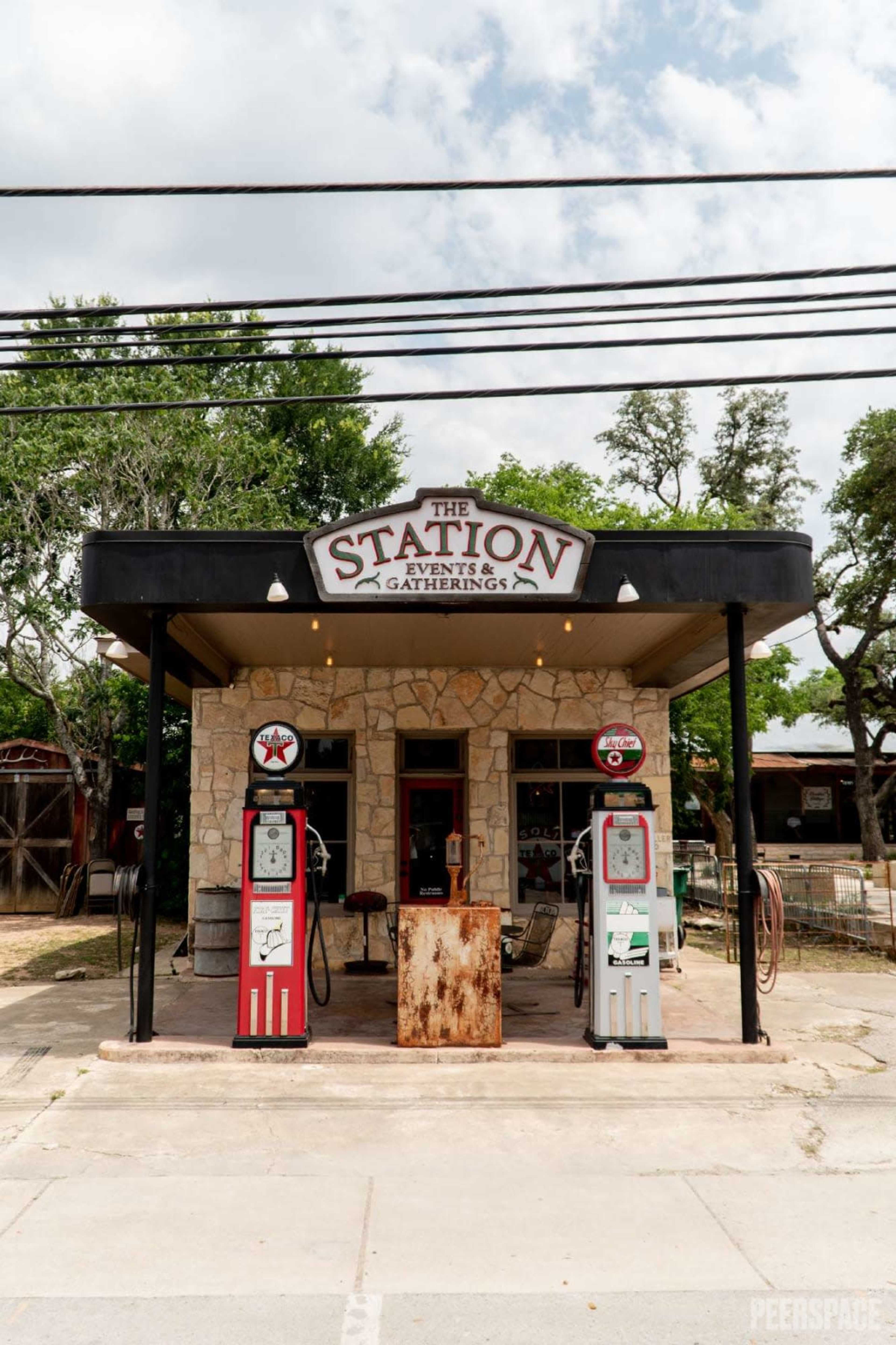 The image shows a vintage gas station building with two gas pumps in front and a sign that reads "The Station Events & Gatherings."