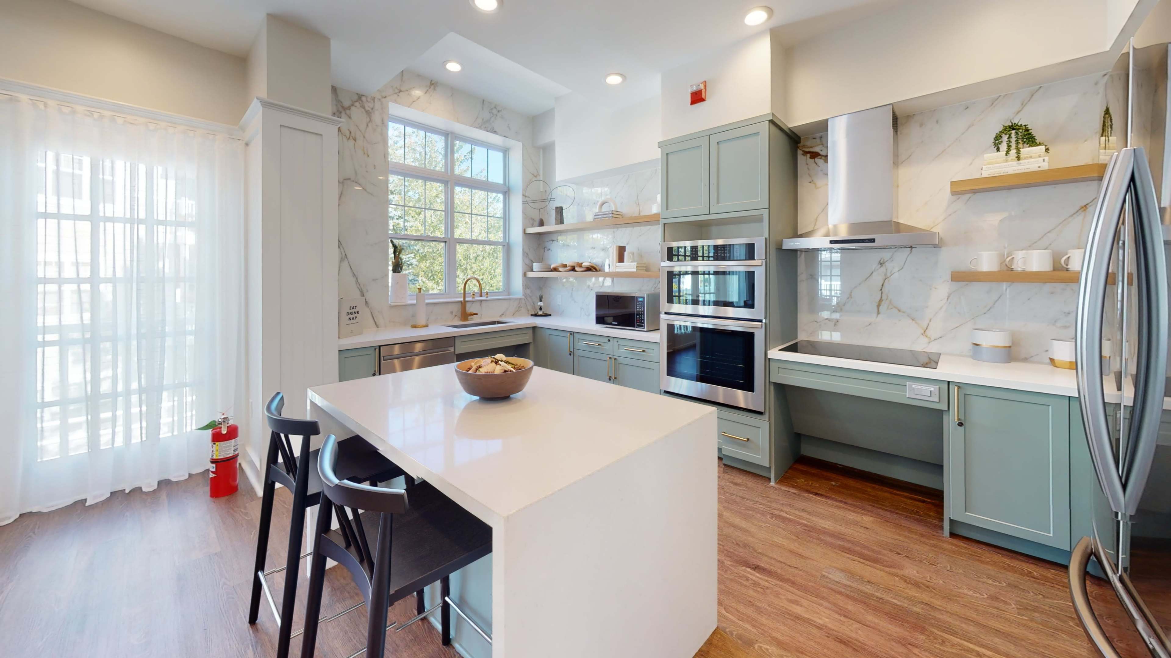 A modern kitchen featuring light blue cabinets, a large white island, and stainless steel appliances.