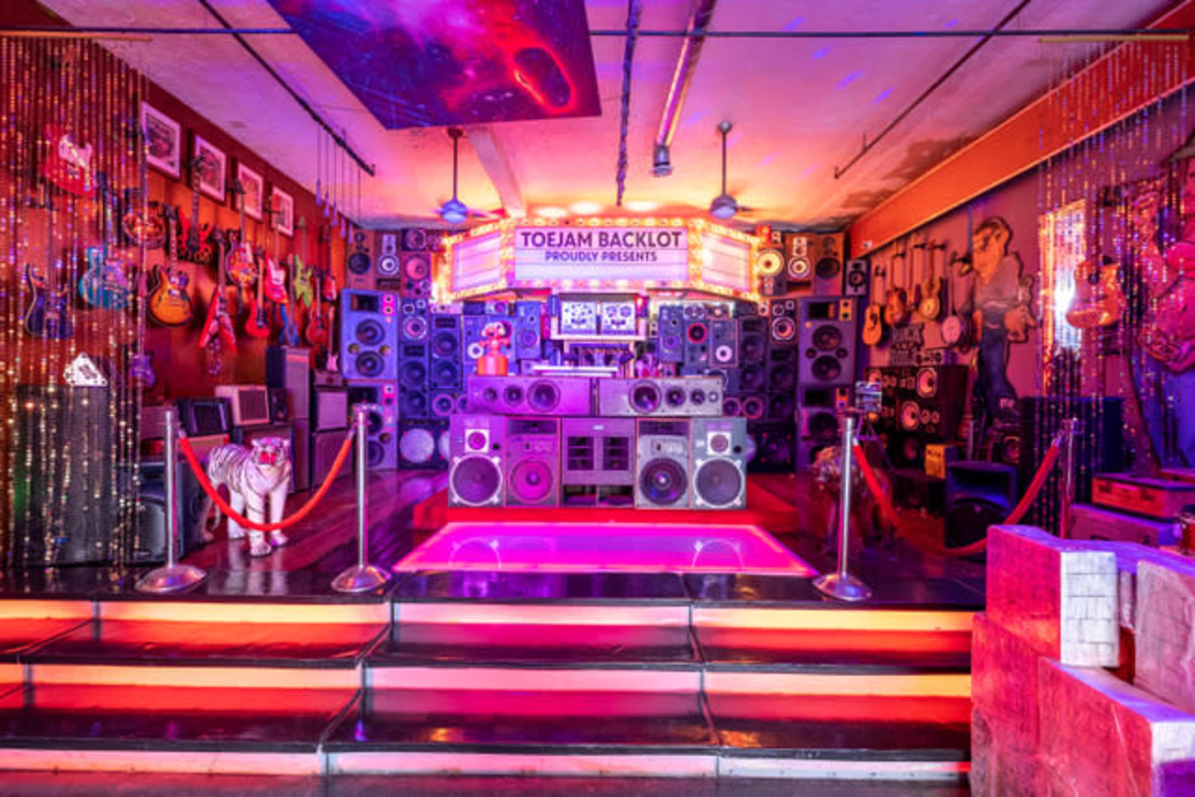 A vibrant music venue featuring an array of guitars, speakers, and colorful lights.