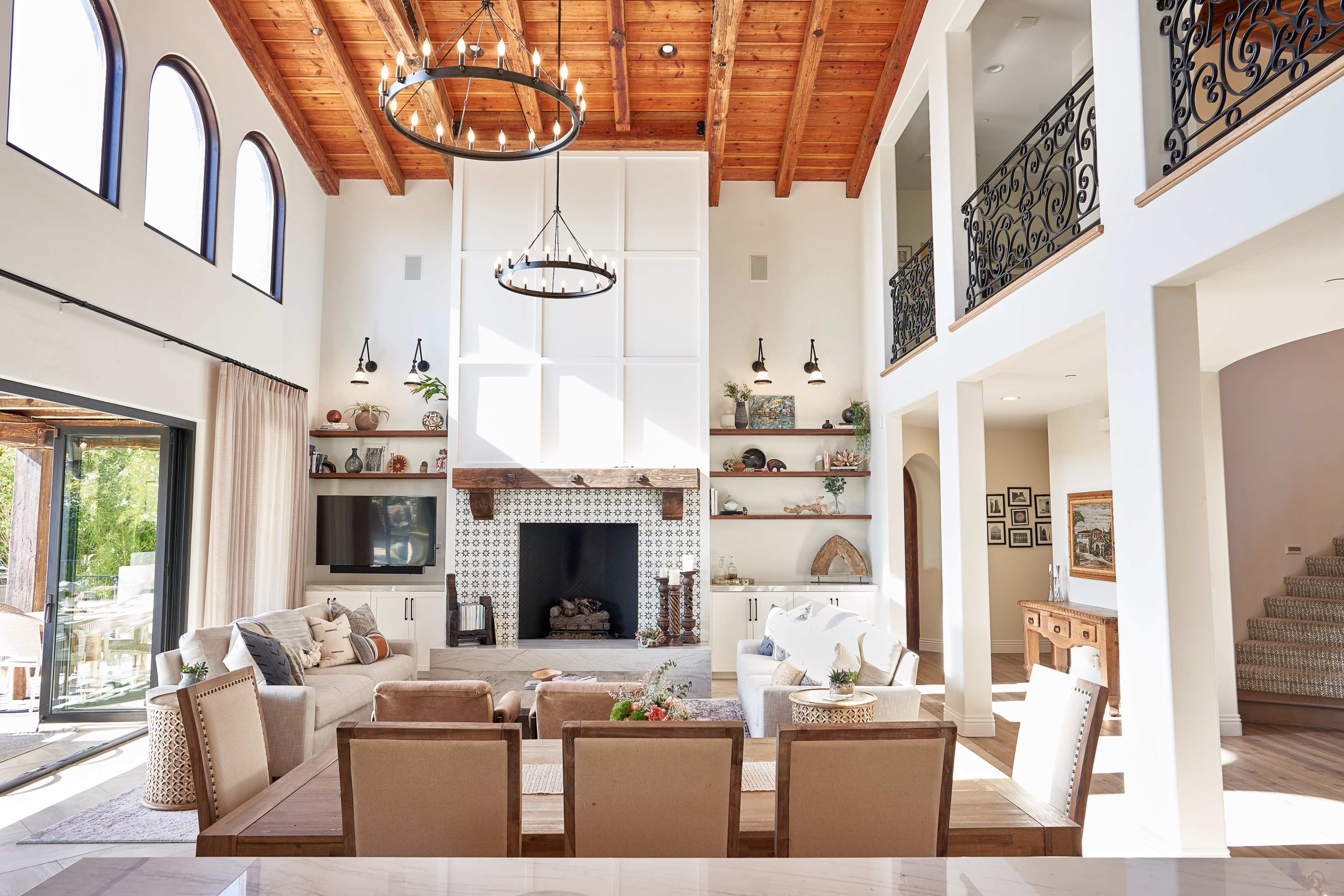 The image shows a spacious, modern living room with a high wooden ceiling, a large fireplace, and comfortable seating arranged around a coffee table.