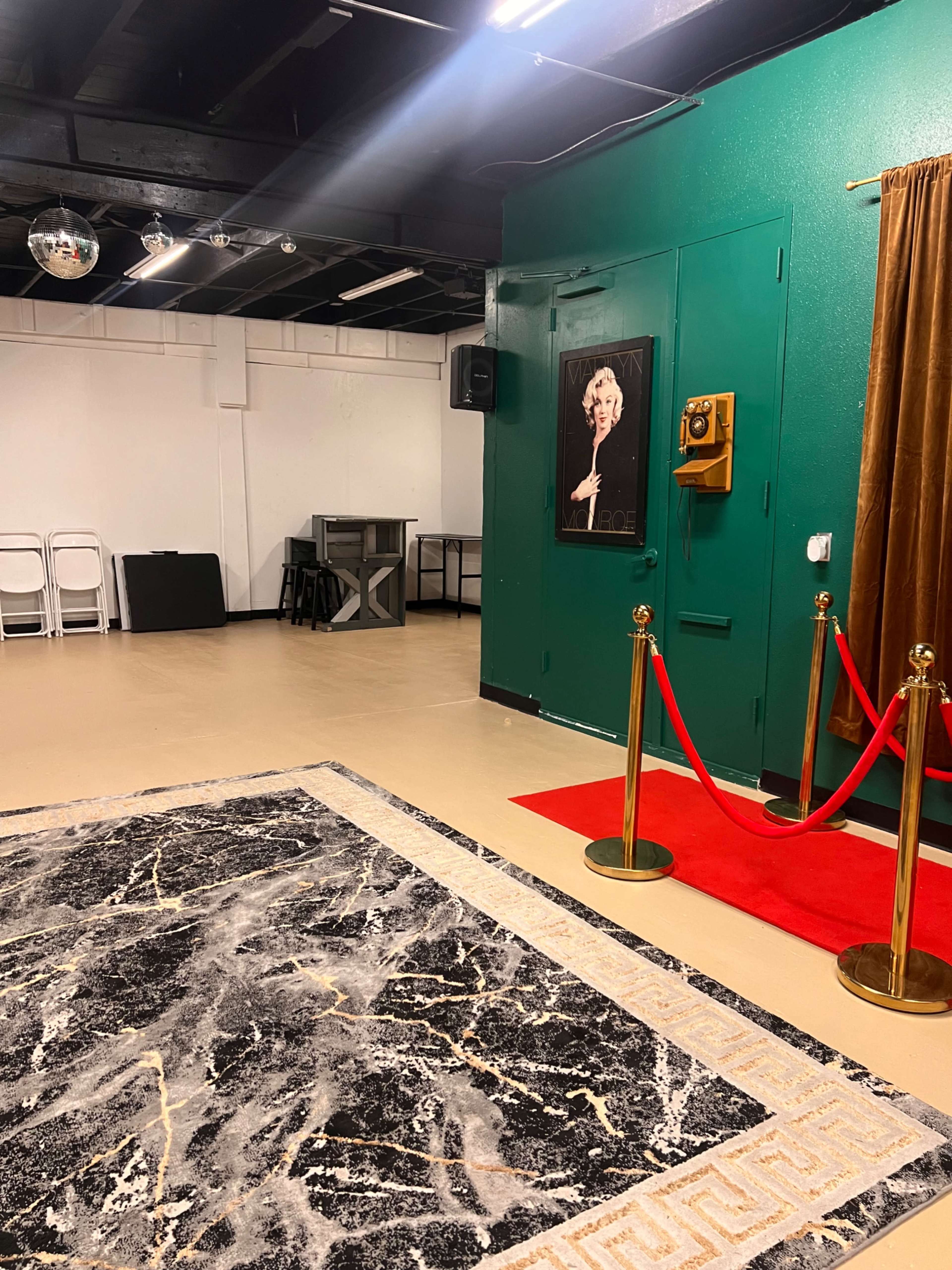 The image shows a stylish indoor space with a green wall, a red carpet leading to a framed artwork, and a gold rope barrier.
