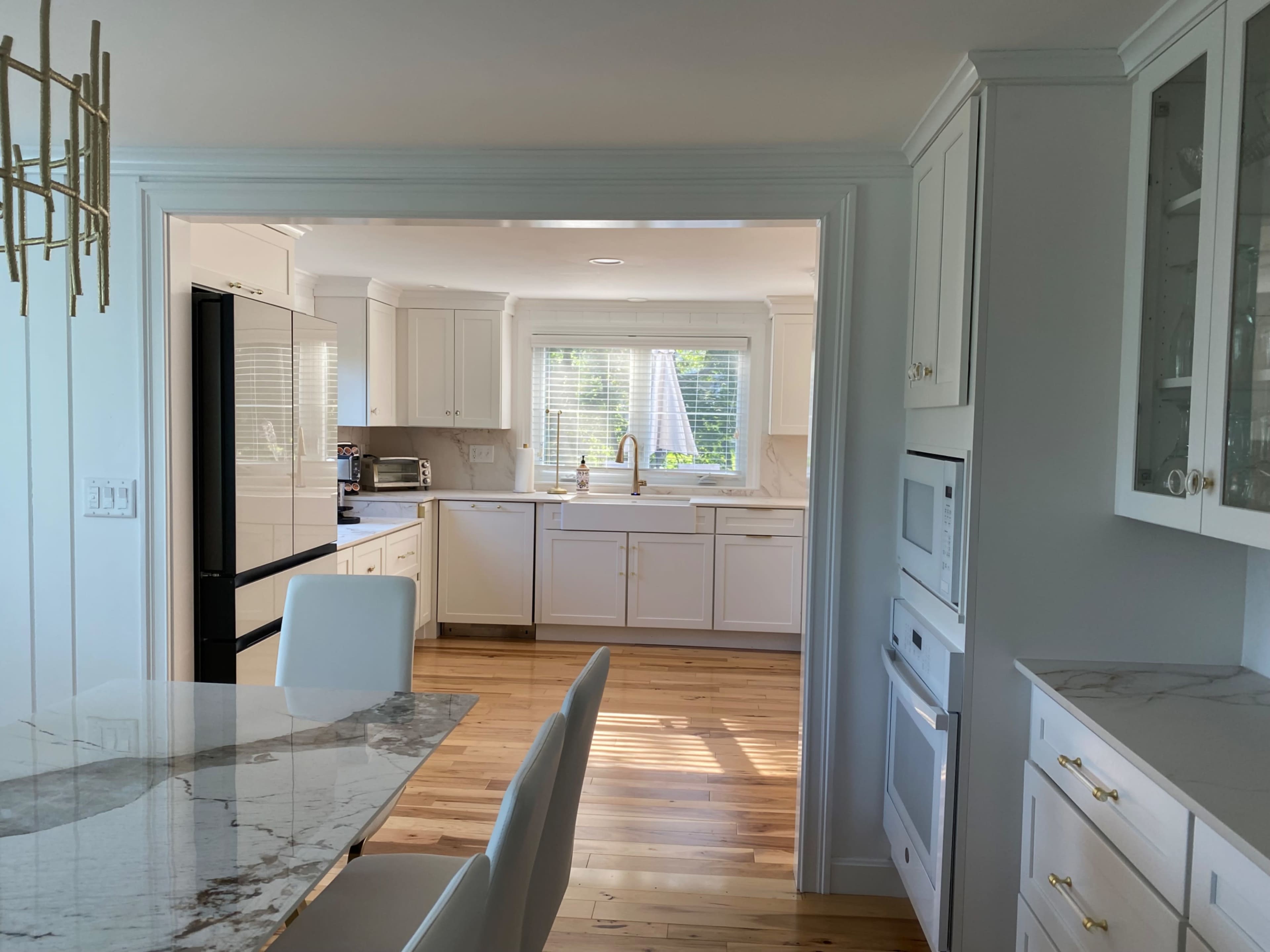 A bright, modern kitchen features white cabinetry, a large island with a marble top, and hardwood flooring.