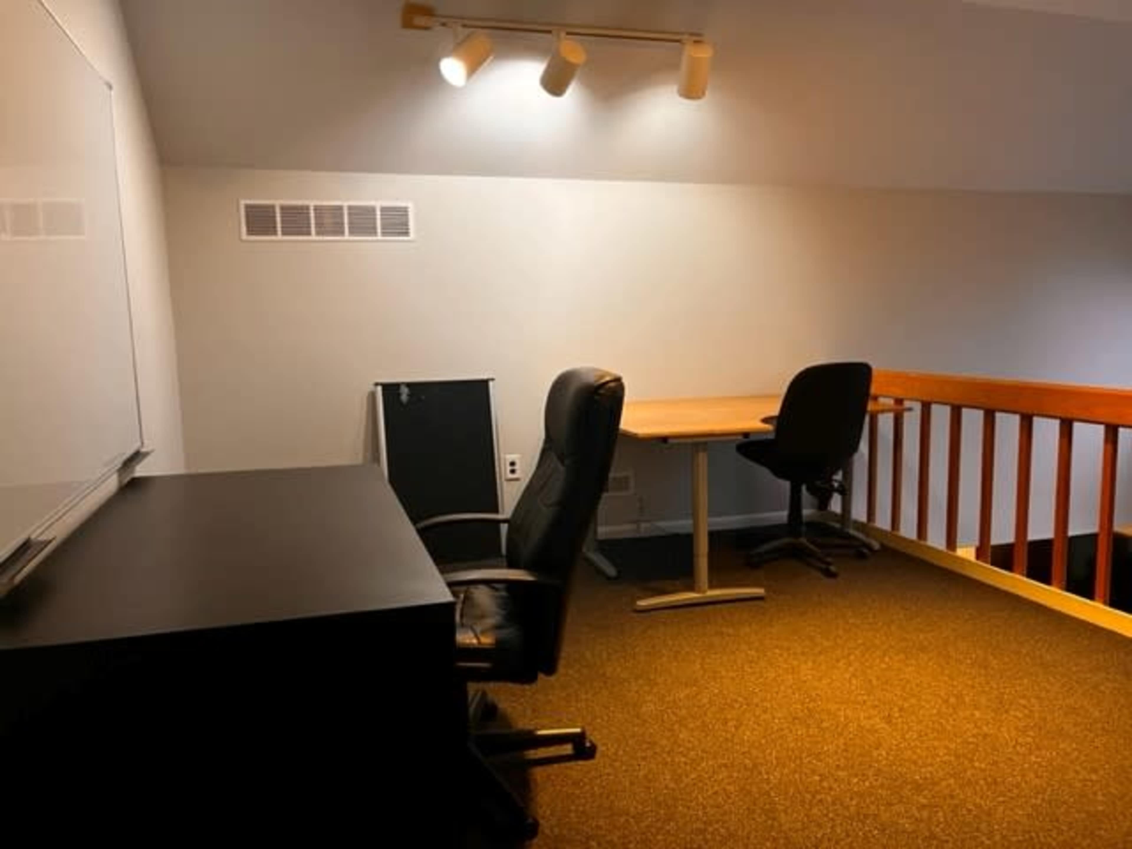 A simple workspace with two chairs, a desk, and a whiteboard in a well-lit loft area.