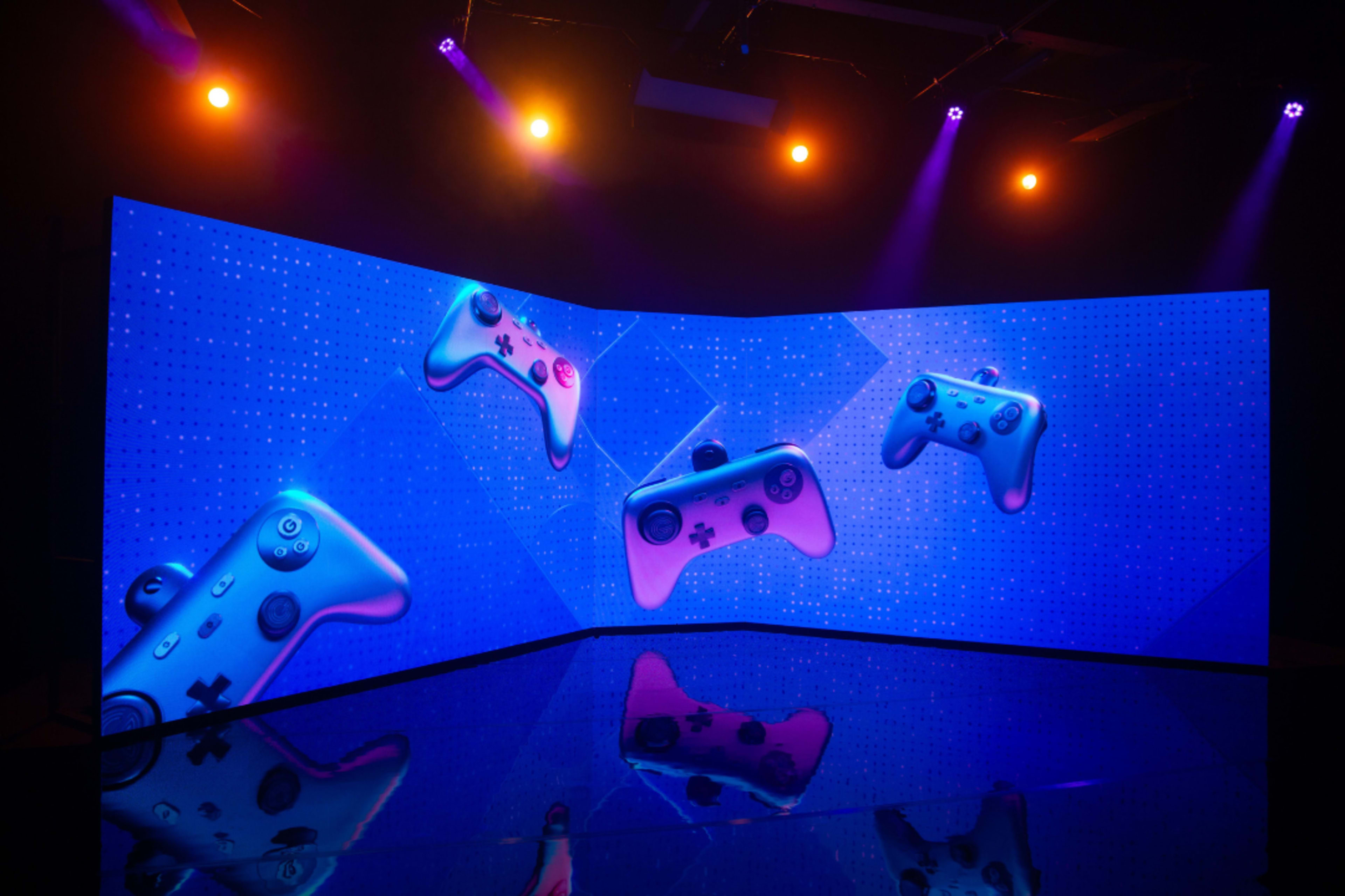 A large display screen showcases various gaming controllers against a blue background with vibrant lights.