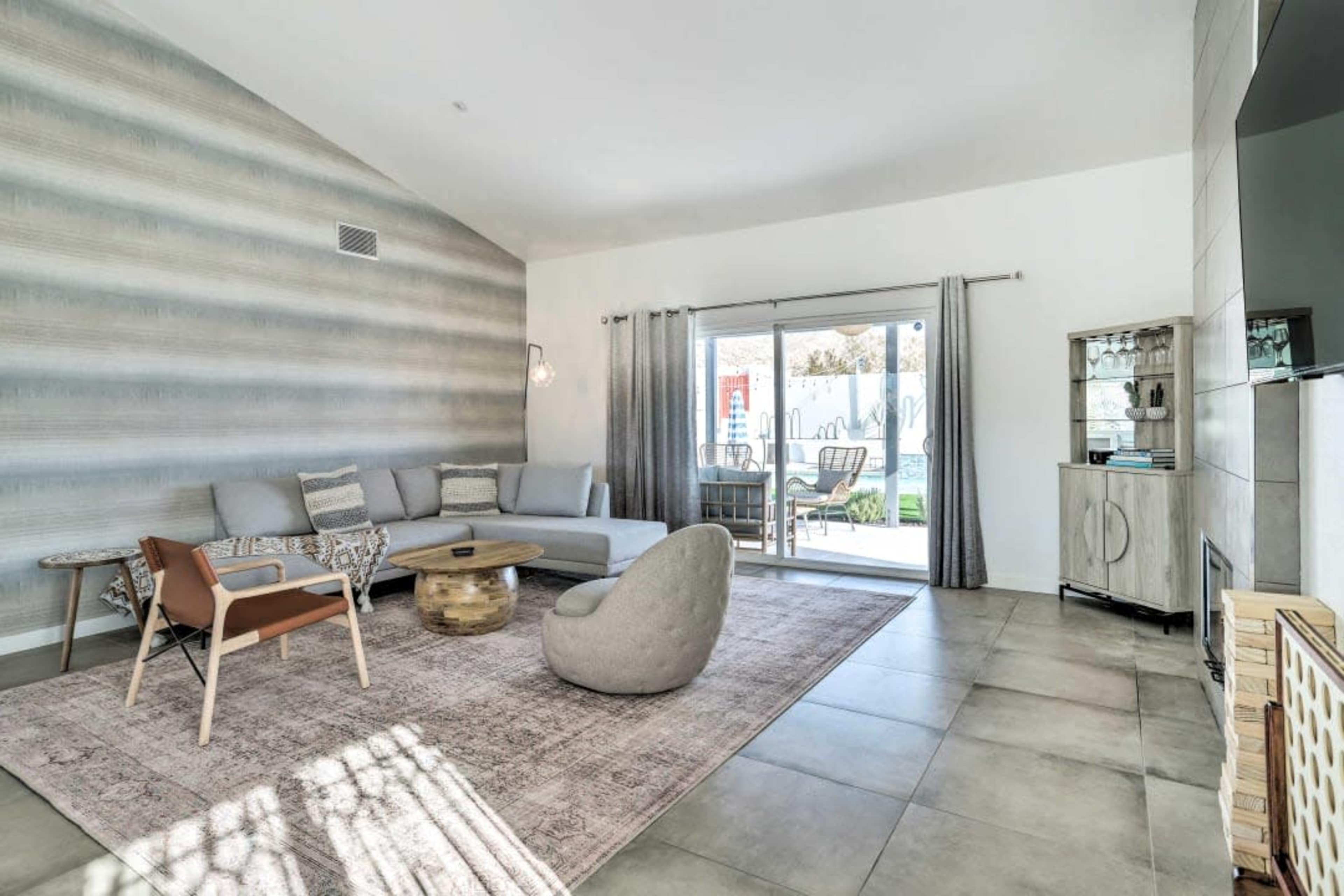 A modern living room features a sectional sofa, a round table, and large windows that overlook an outdoor patio area.