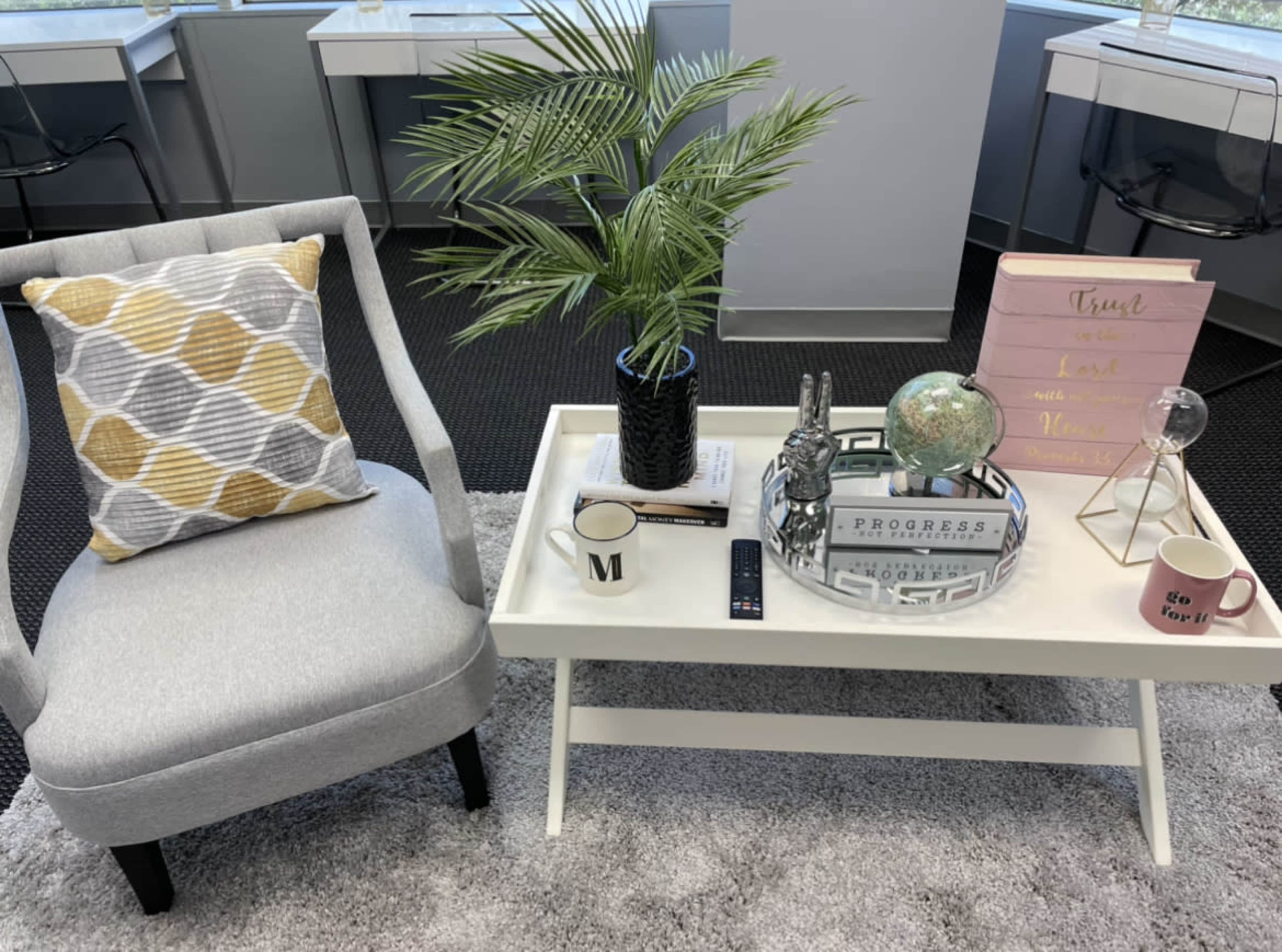 A light gray armchair with a patterned cushion sits beside a white coffee table adorned with decorative items, including a potted plant and a globe.