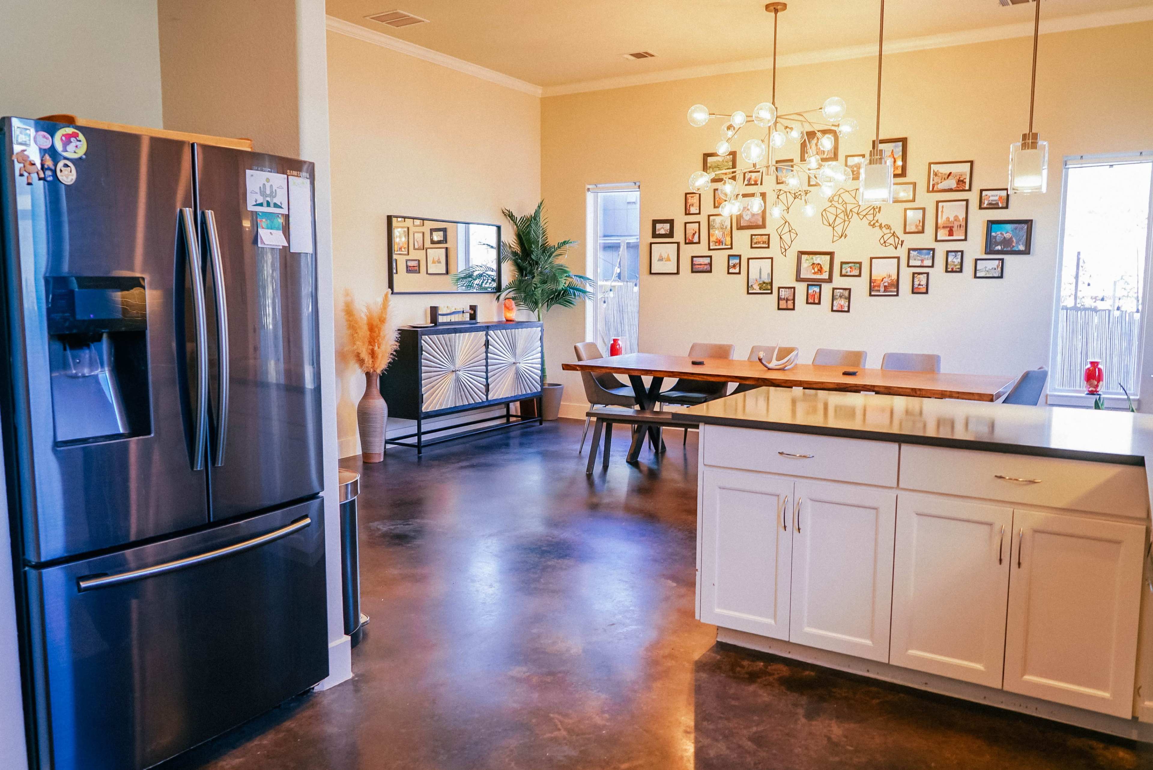A modern kitchen and dining area with a stainless steel refrigerator, a large wooden dining table, and walls decorated with a collage of framed pictures.