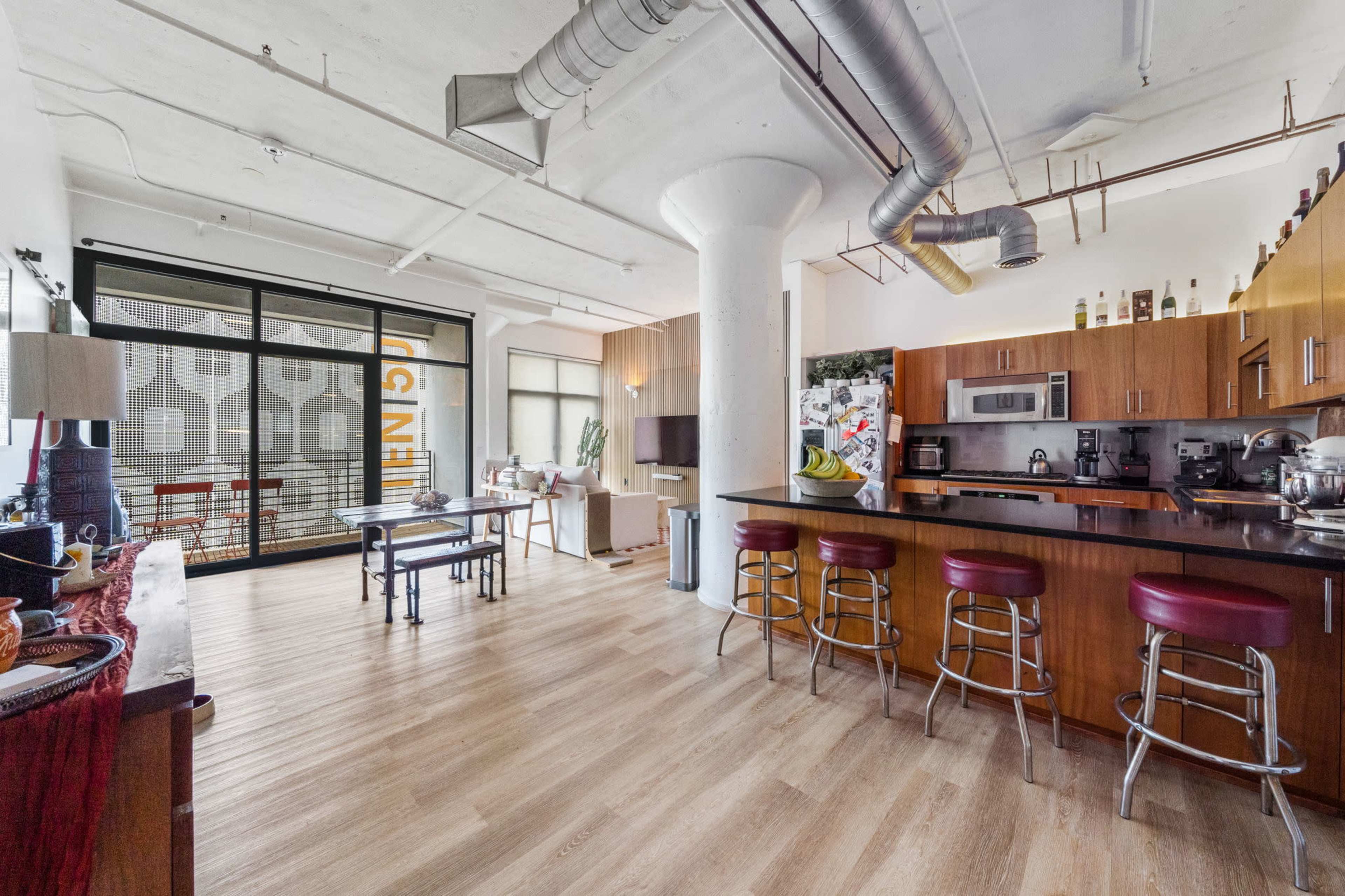 The image shows a spacious, modern open-concept living area that includes a kitchen with bar seating, a dining table, and large windows allowing for ample natural light.