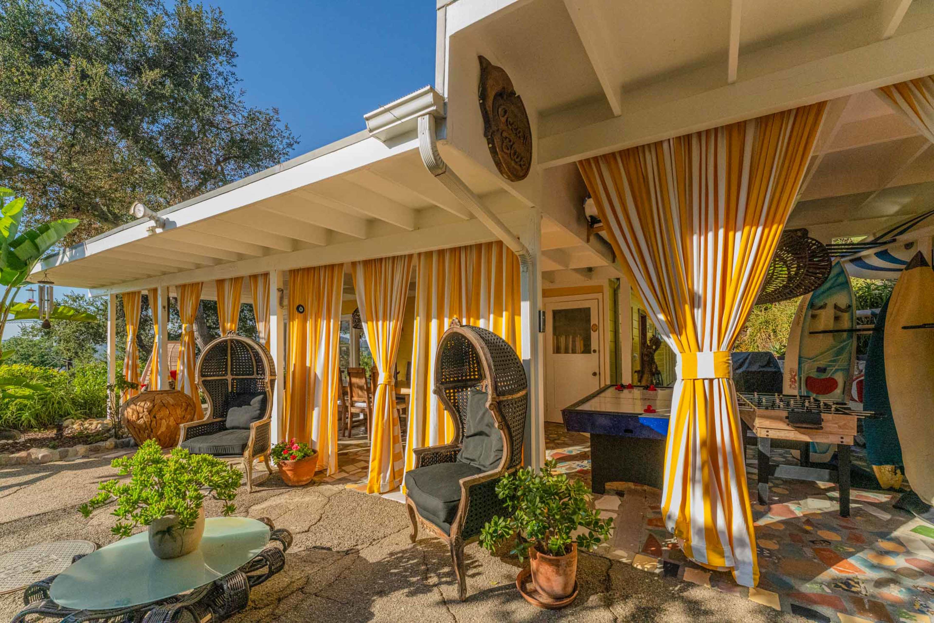 A patio area with yellow and white striped curtains, two wicker chairs, and a circular table surrounded by potted plants.