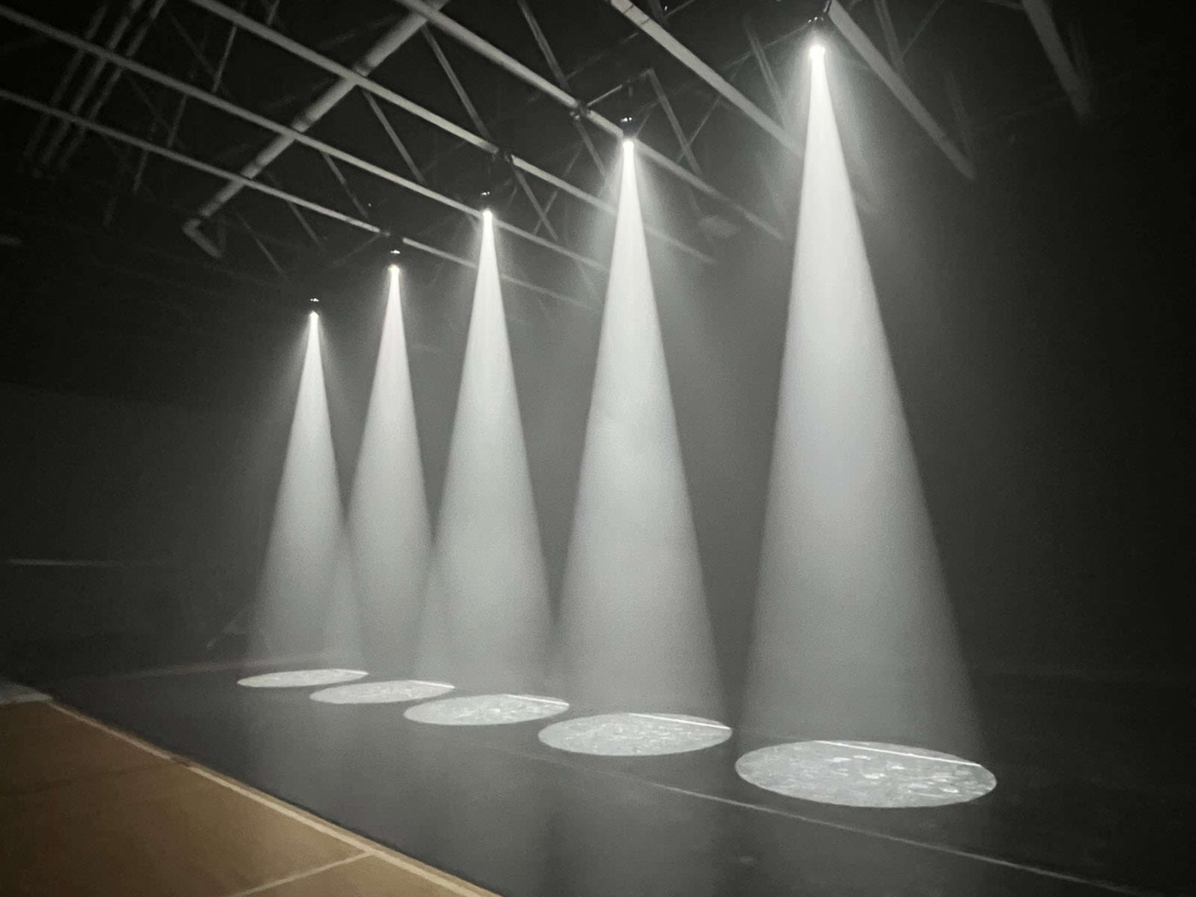 Five focused light beams illuminate circular patches on a dark stage.