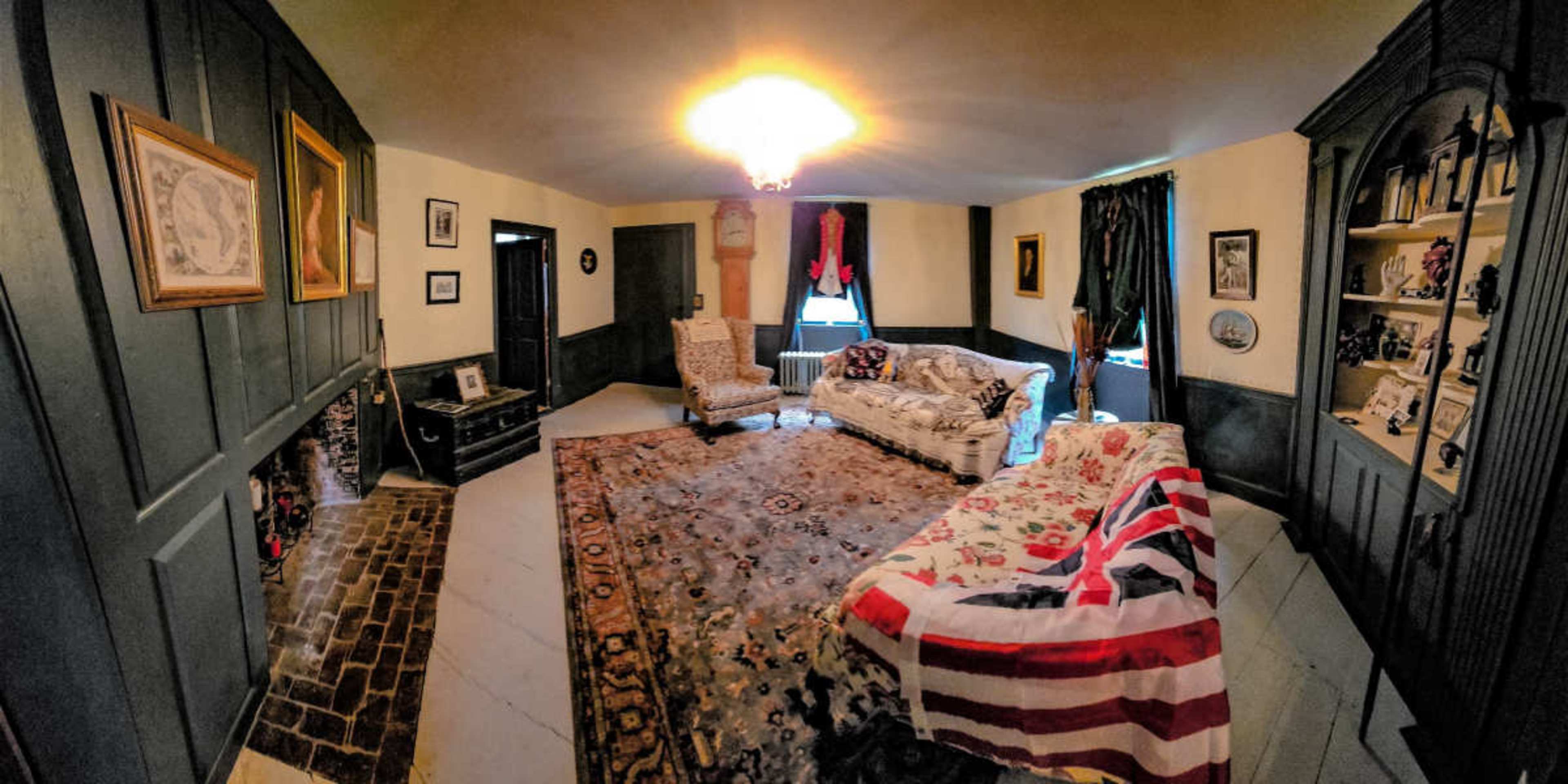The image shows a spacious living room with patterned furniture, a large area rug, and a decorative bookshelf against a dark paneled wall.
