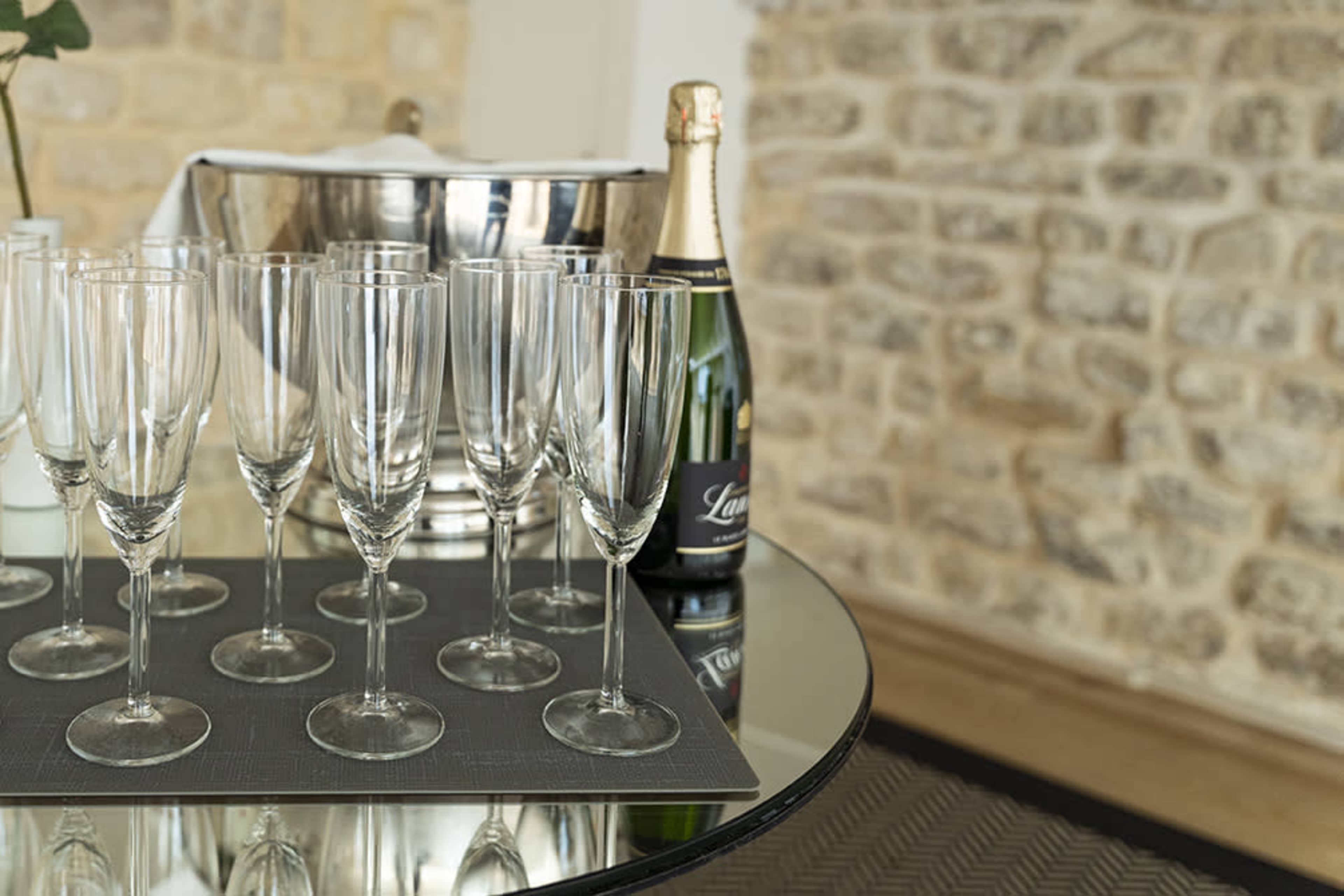 A set of champagne flutes is arranged on a mirrored table next to a bottle of champagne and an ice bucket, against a stone wall backdrop.