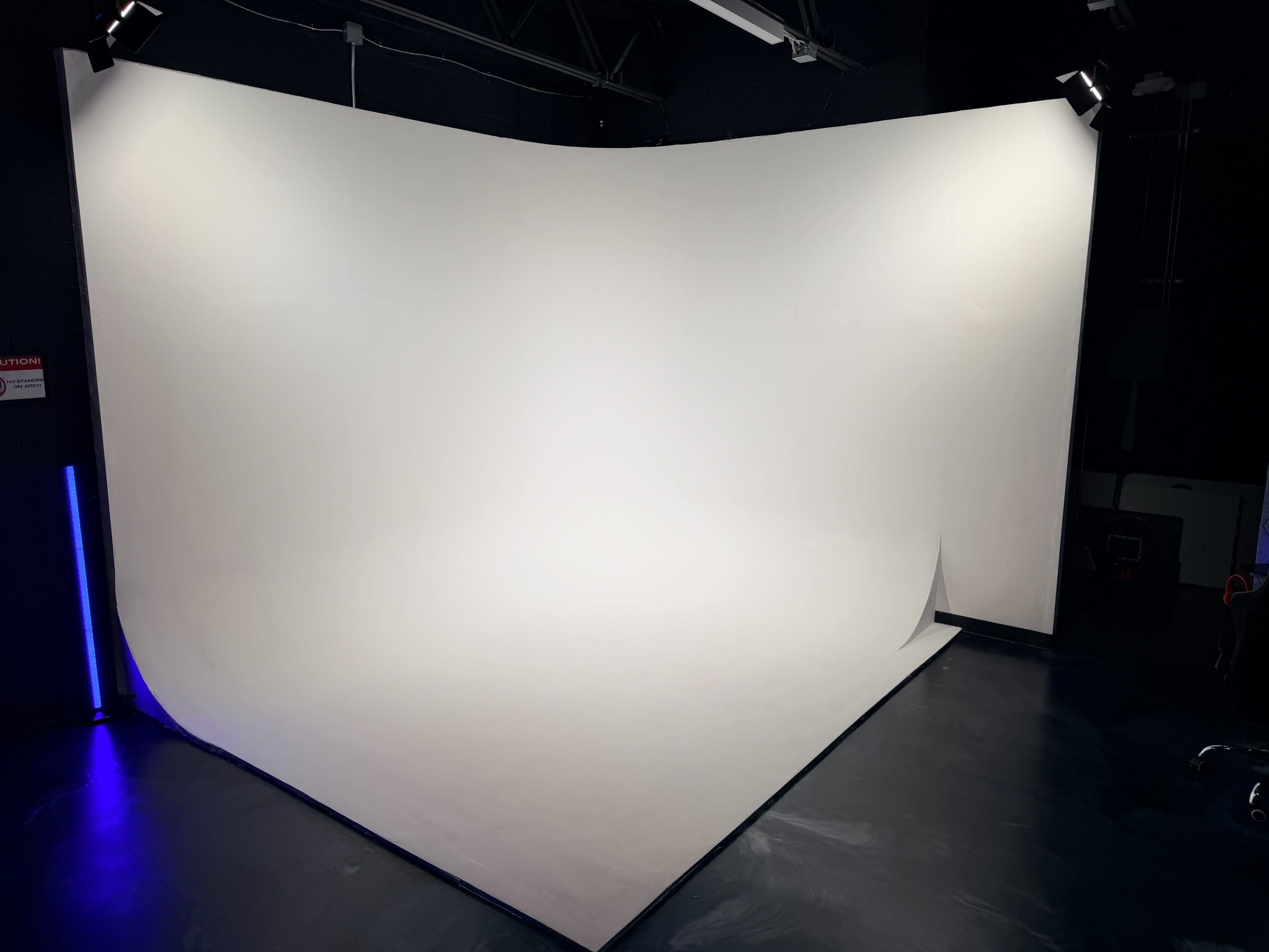 The image shows a blank photo studio with a curved, seamless white backdrop and dark flooring.