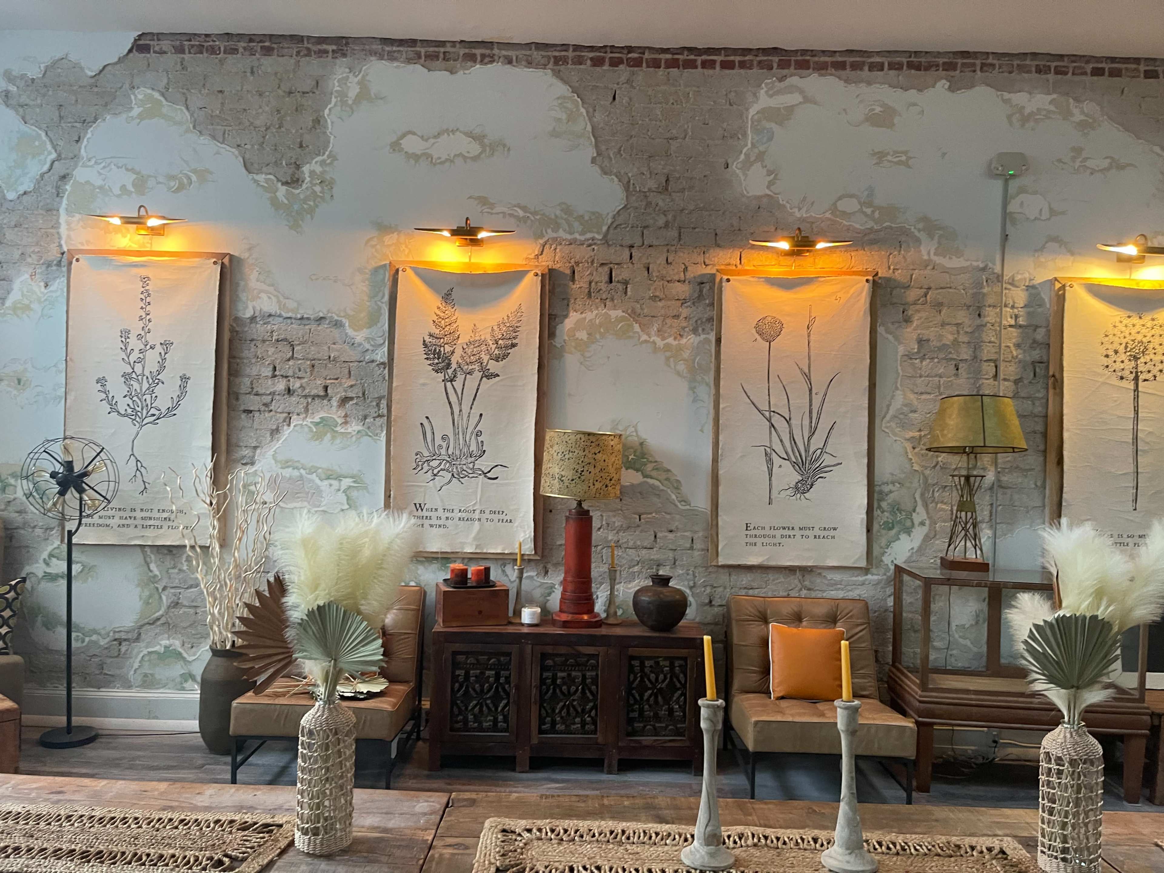 A vintage-inspired interior with exposed brick walls, framed botanical prints, a wooden side table, and decorative vases on a wooden surface.